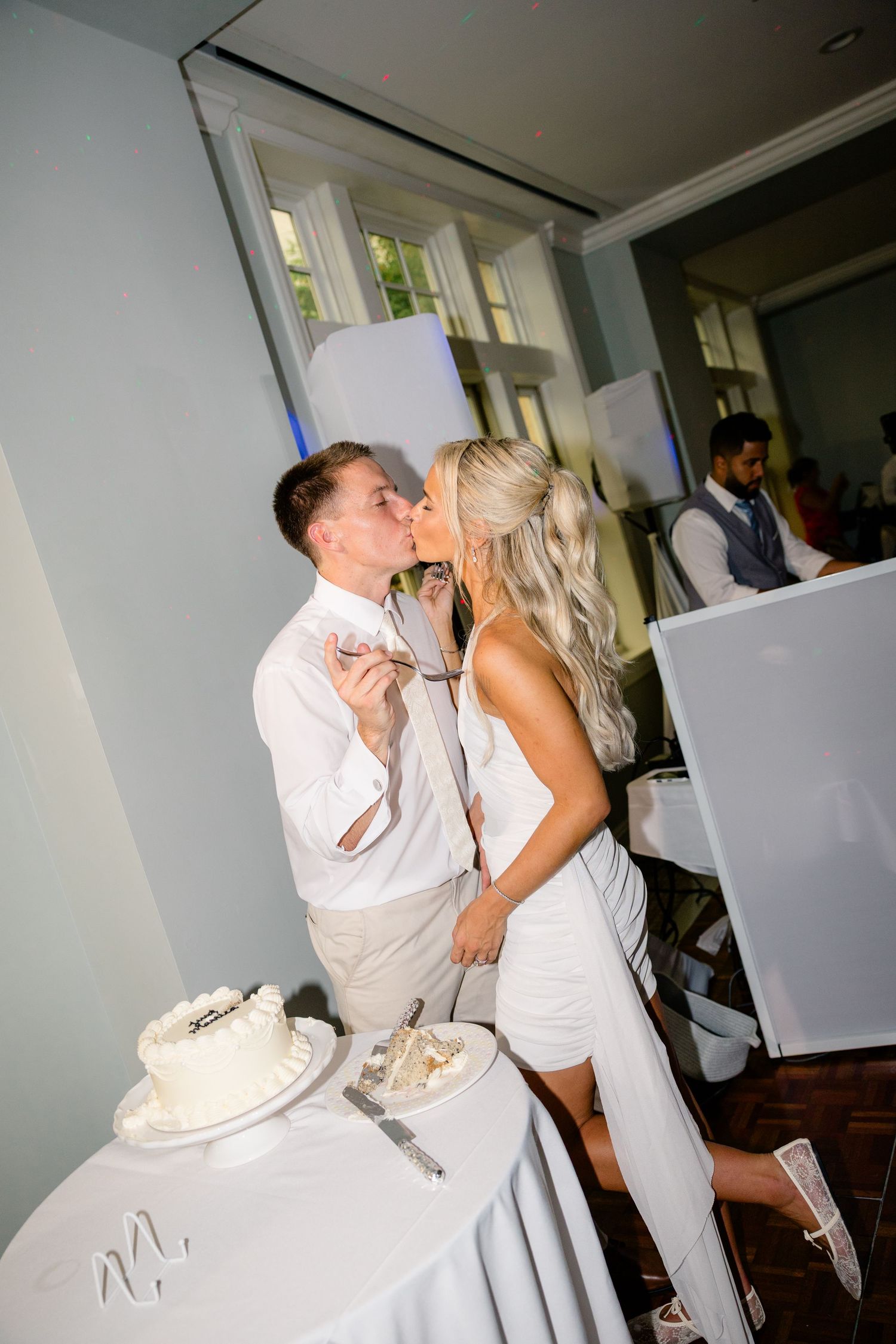Bride and groom share a kiss while cutting their white wedding cake at the reception.