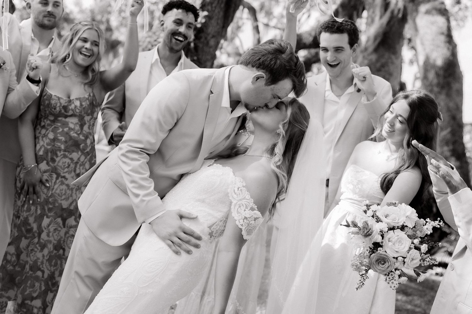 Wedding party members celebrate outdoors with joyful expressions and formal attire.