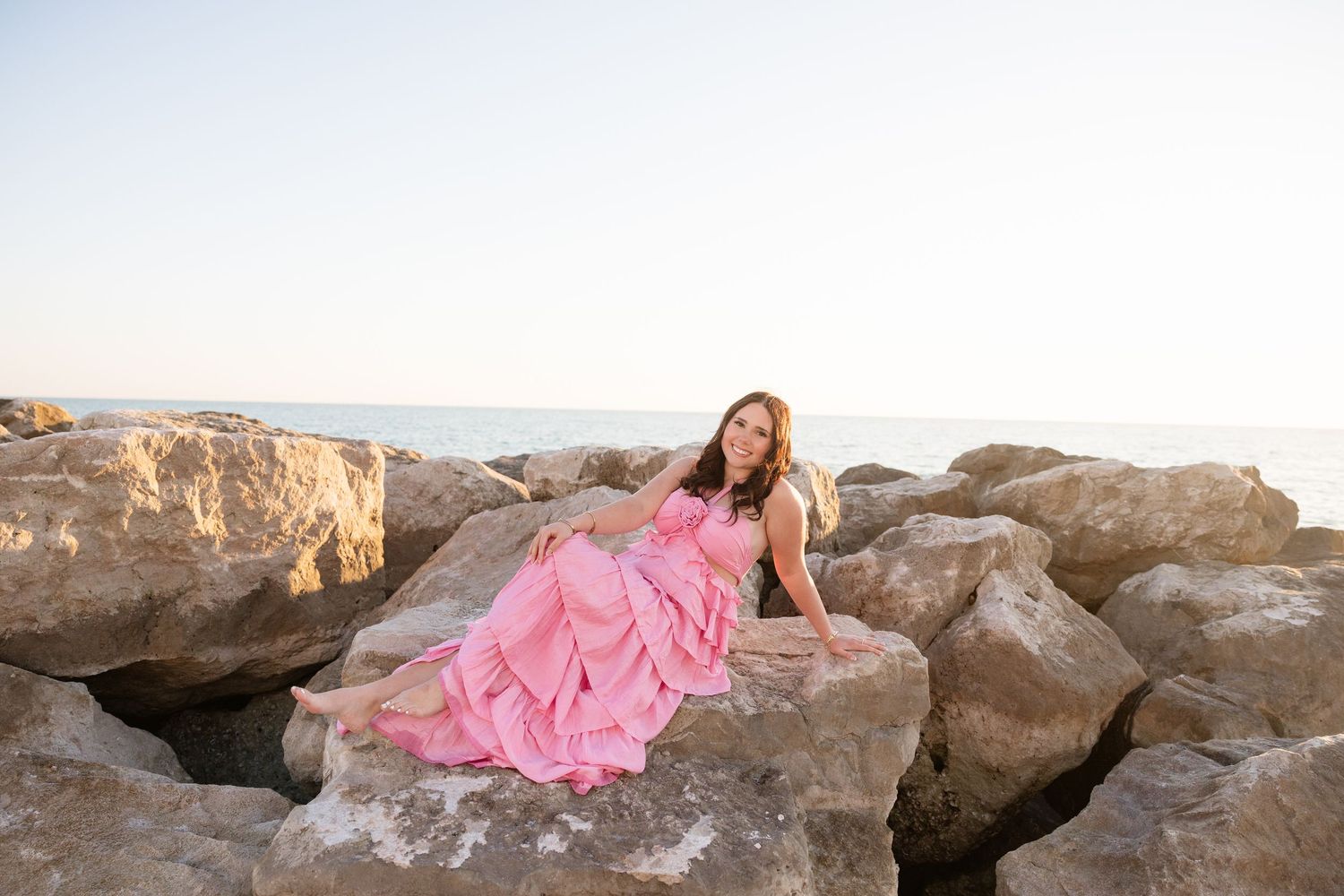 Senior portrait in a pink gown on coastal rocks at sunset during a Florida beach senior photography session.