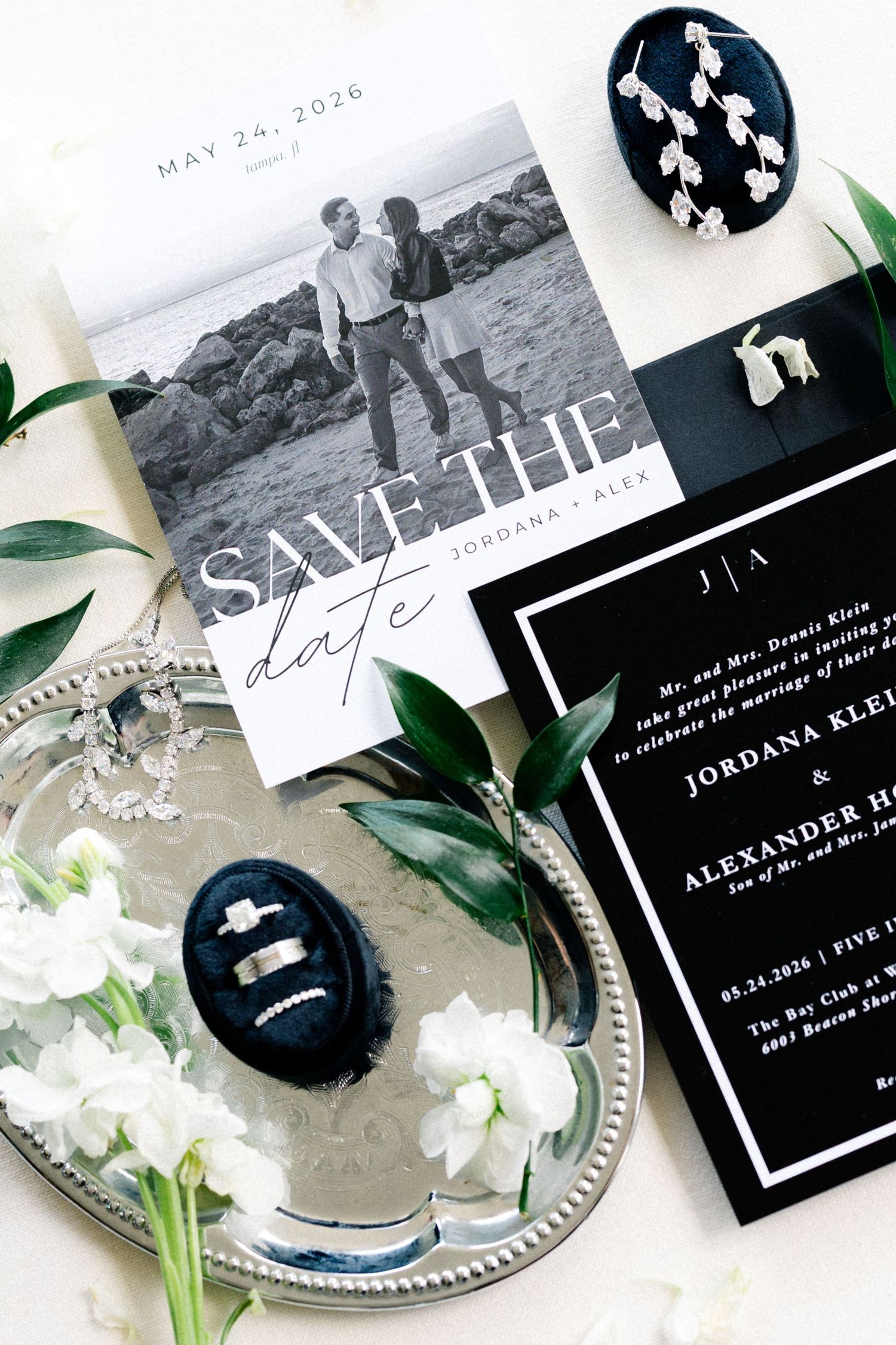 Black and white wedding stationery suite with save the date, invitation, rings, and white florals on silver tray.