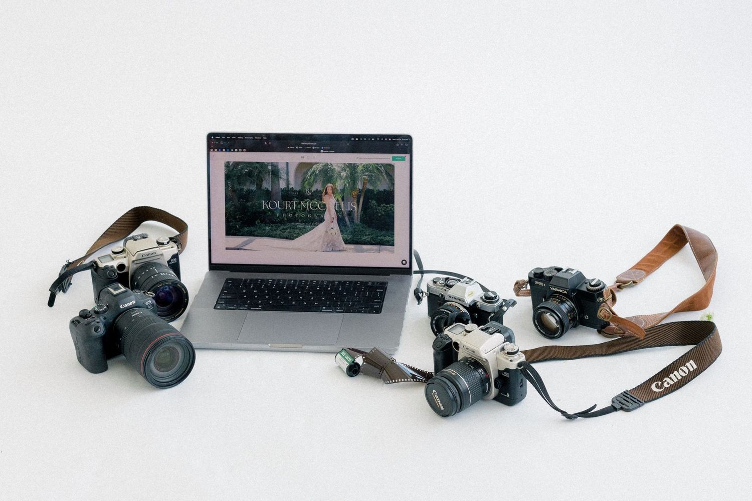 Canon DSLR cameras with straps surround an open laptop displaying a wedding photography website on white background.