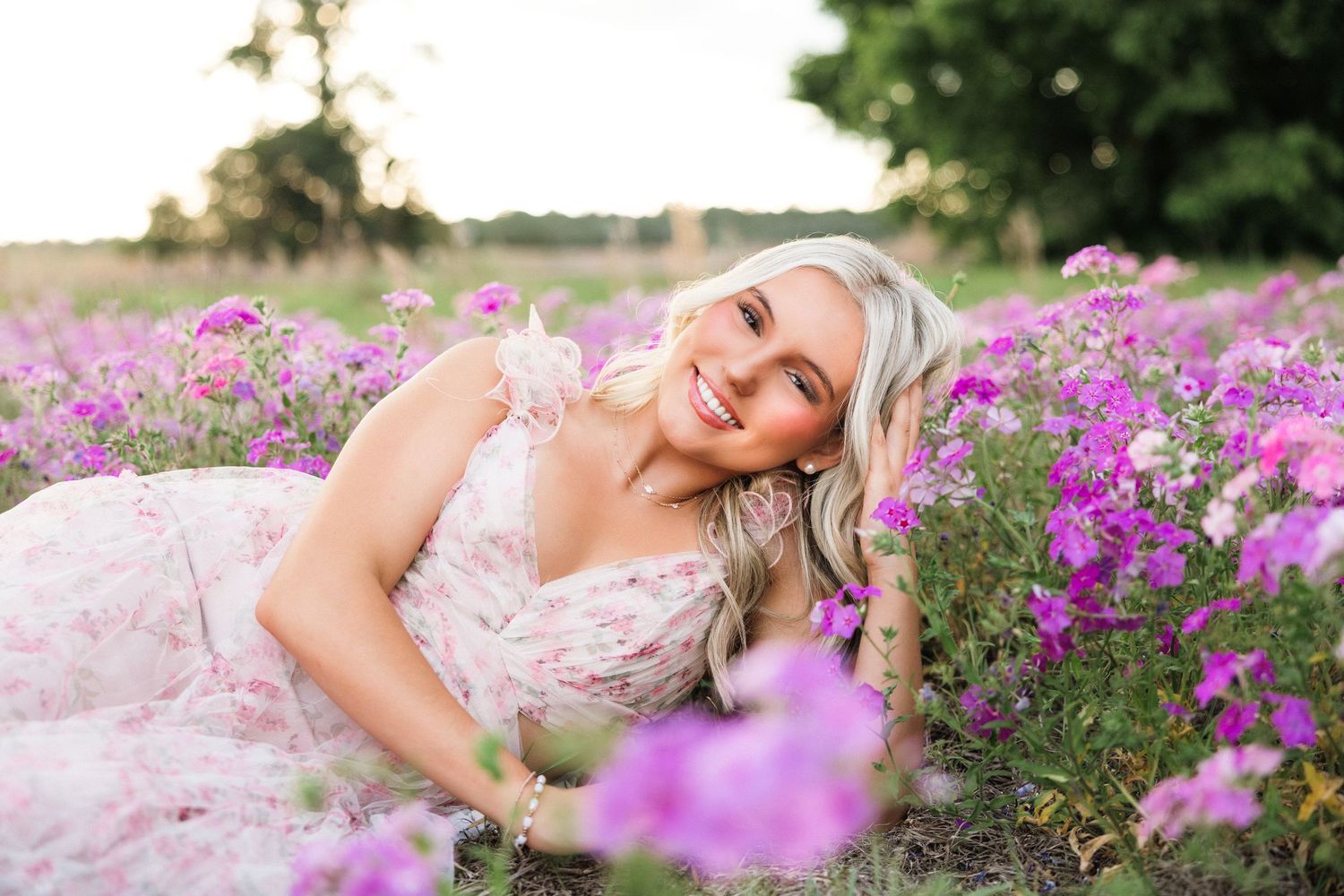 Florida senior portrait in pink floral dress surrounded by purple wildflowers at golden hour.