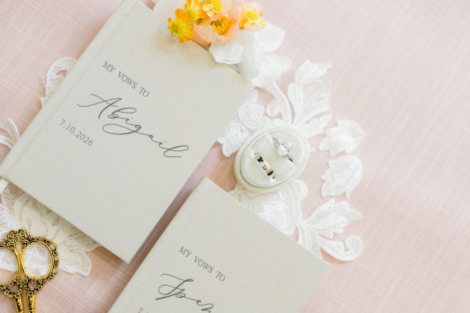 Elegant wedding vow books personalized with bride and groom names, displayed with a ring box and floral accents.