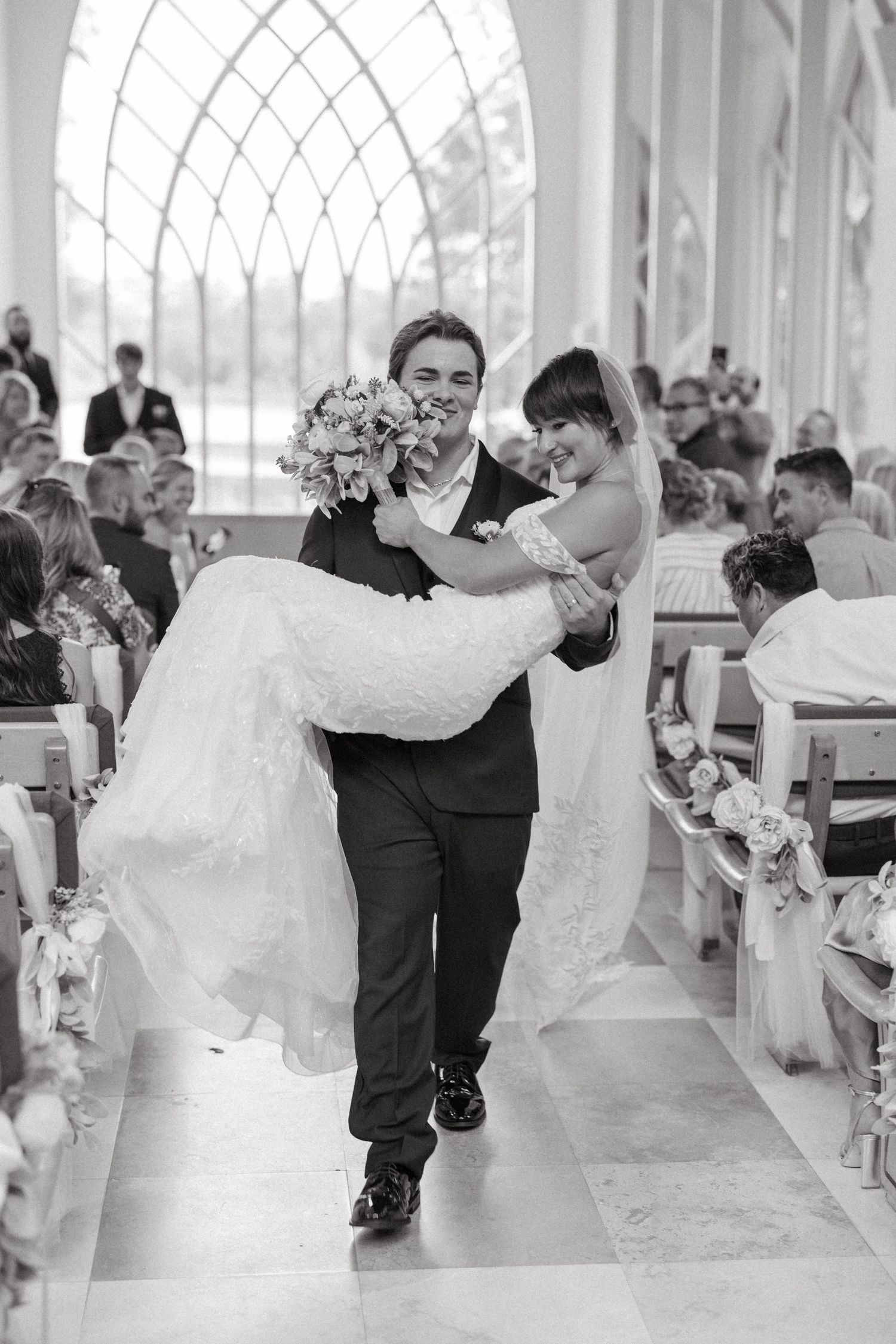 Black and white photo of groom carrying bride down the chapel aisle after their Baughman Center Wedding