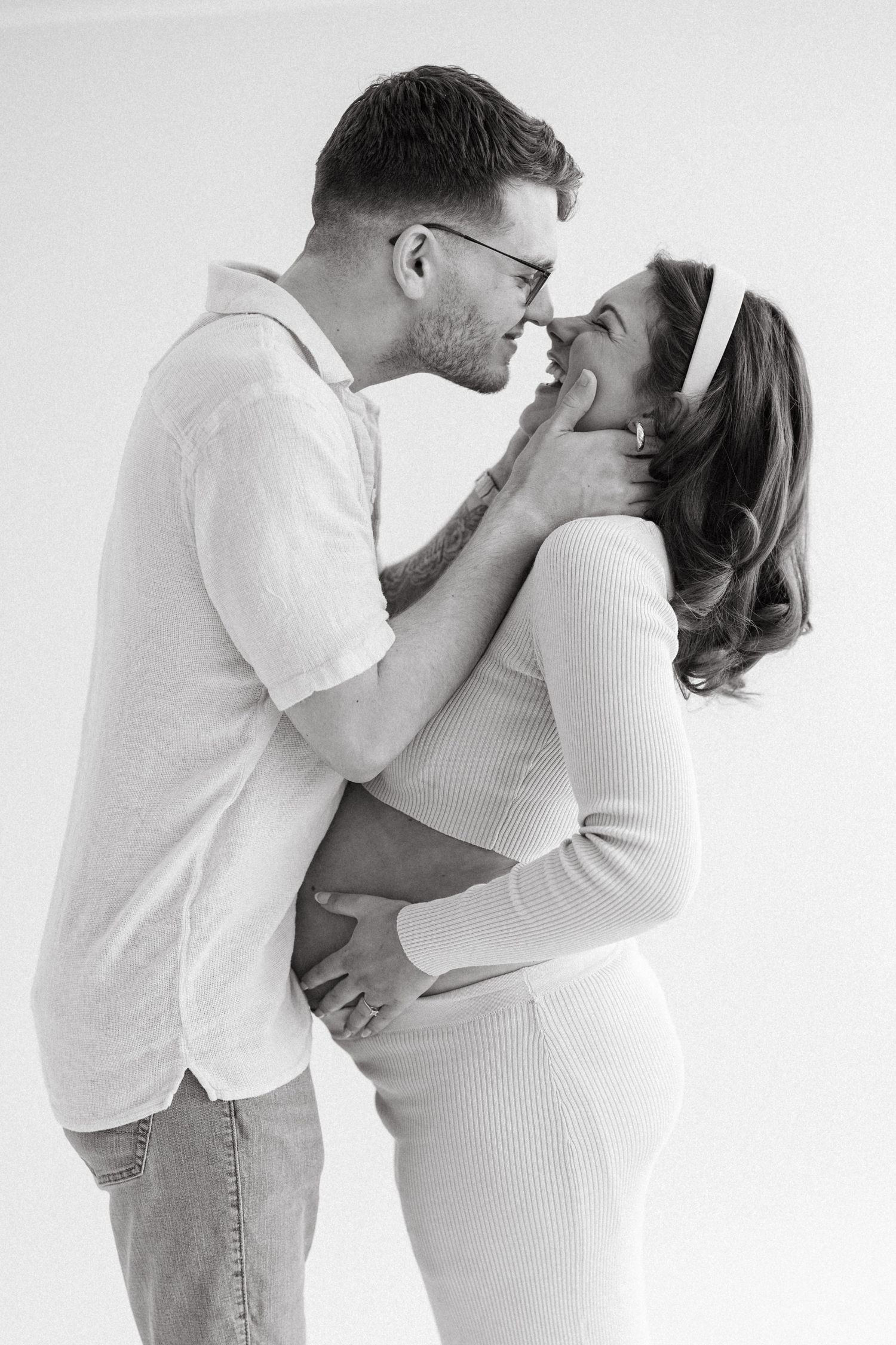 Black and white photo of a couple sharing a tender moment, man gently touching pregnant woman's face as she smiles.