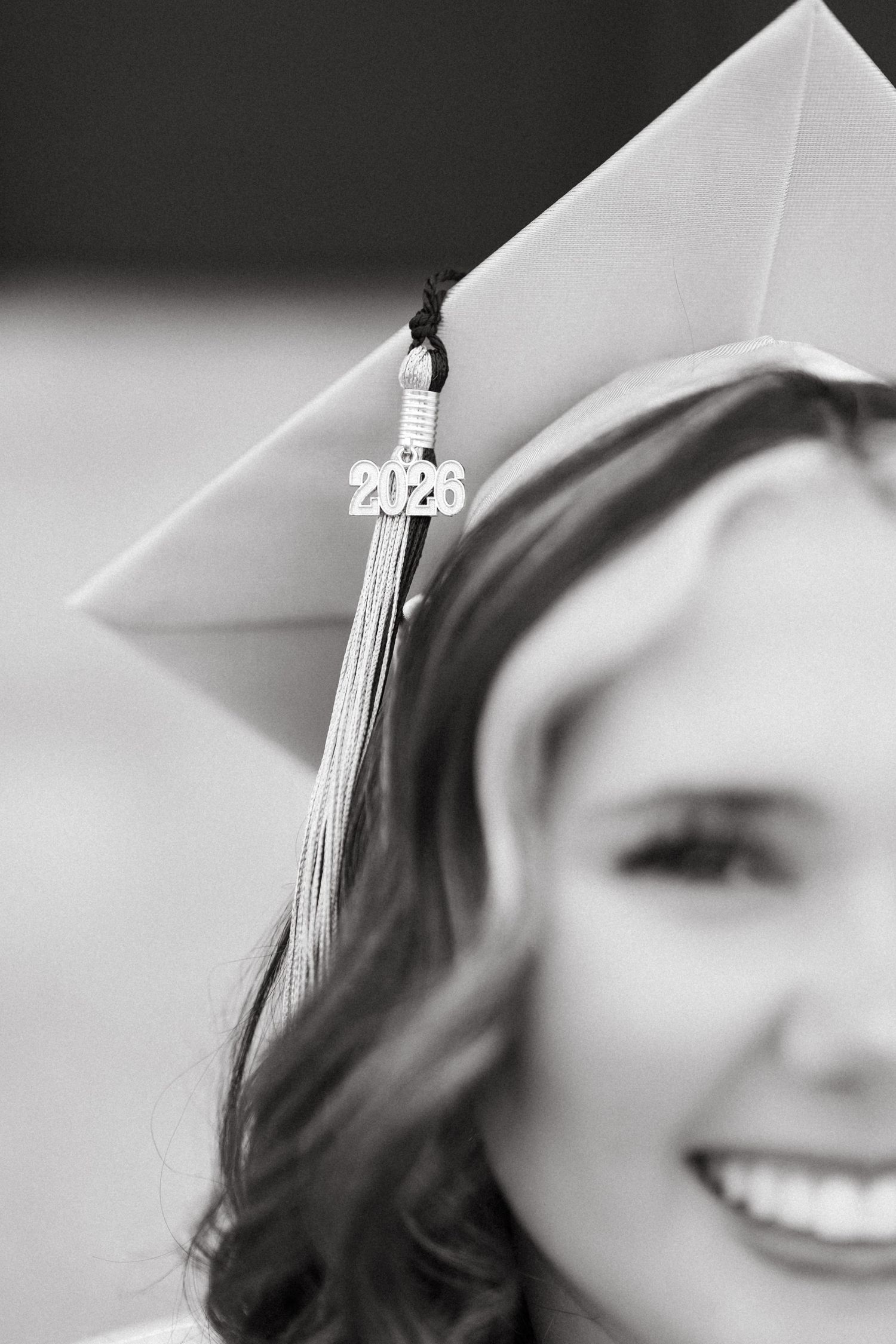 Black and white photo of a smiling graduate wearing a 2026 graduation cap with tassel.