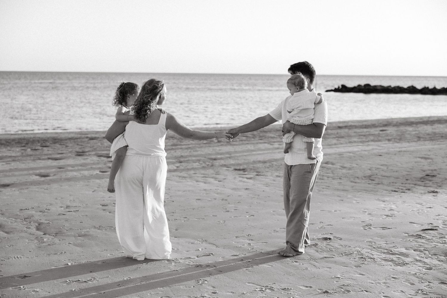 Black and white beach wedding photo of couple holding hands with child on sandy shore near ocean.