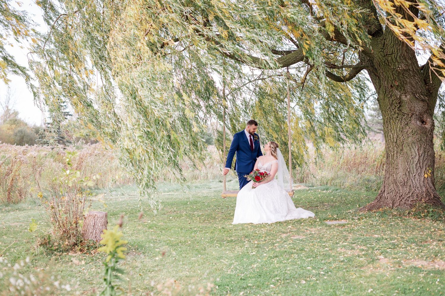 Dreamy wedding portrait under large willow tree in autumn field.