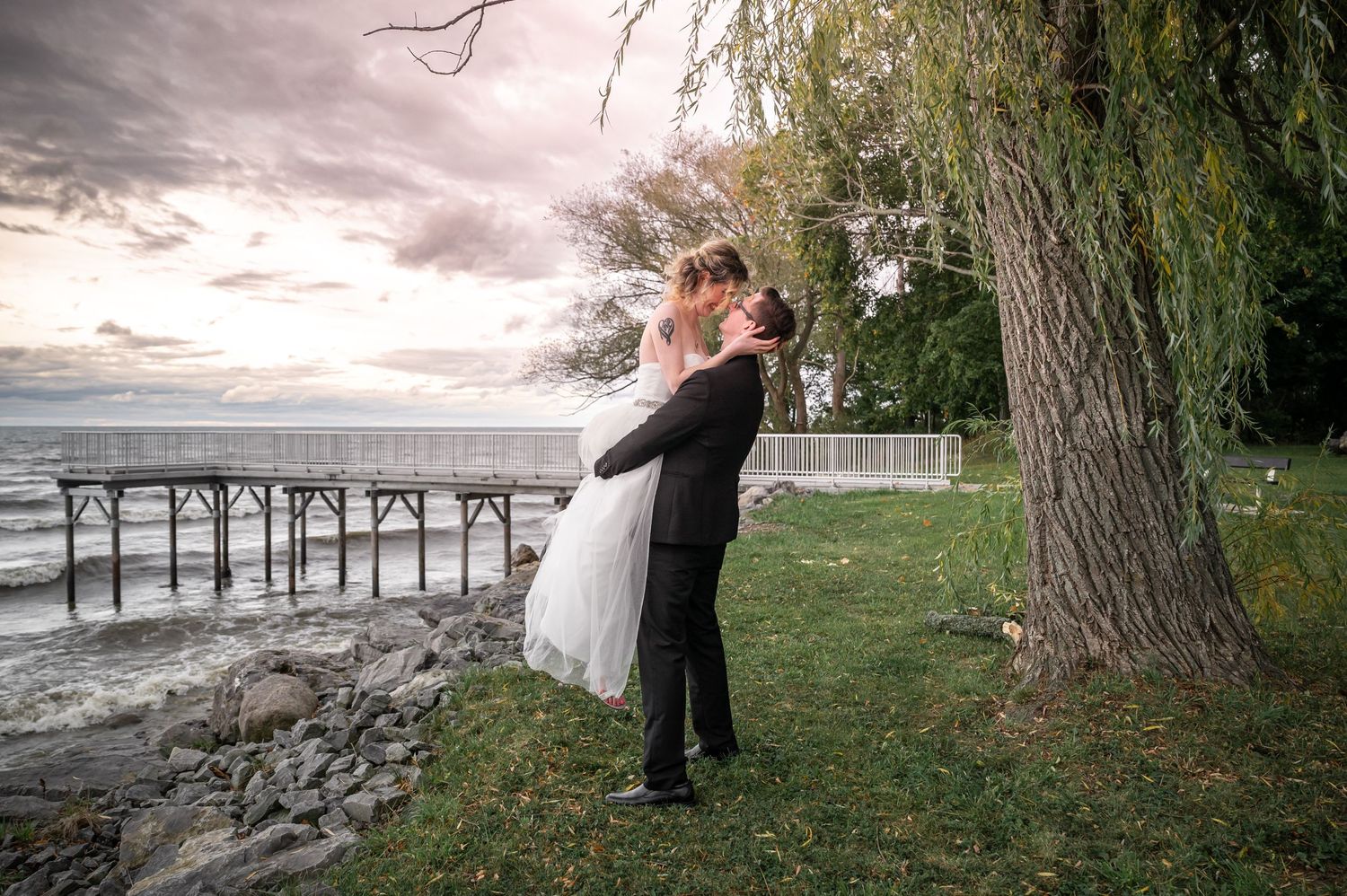 Romantic lift pose during sunset wedding photoshoot by lakeside pier.