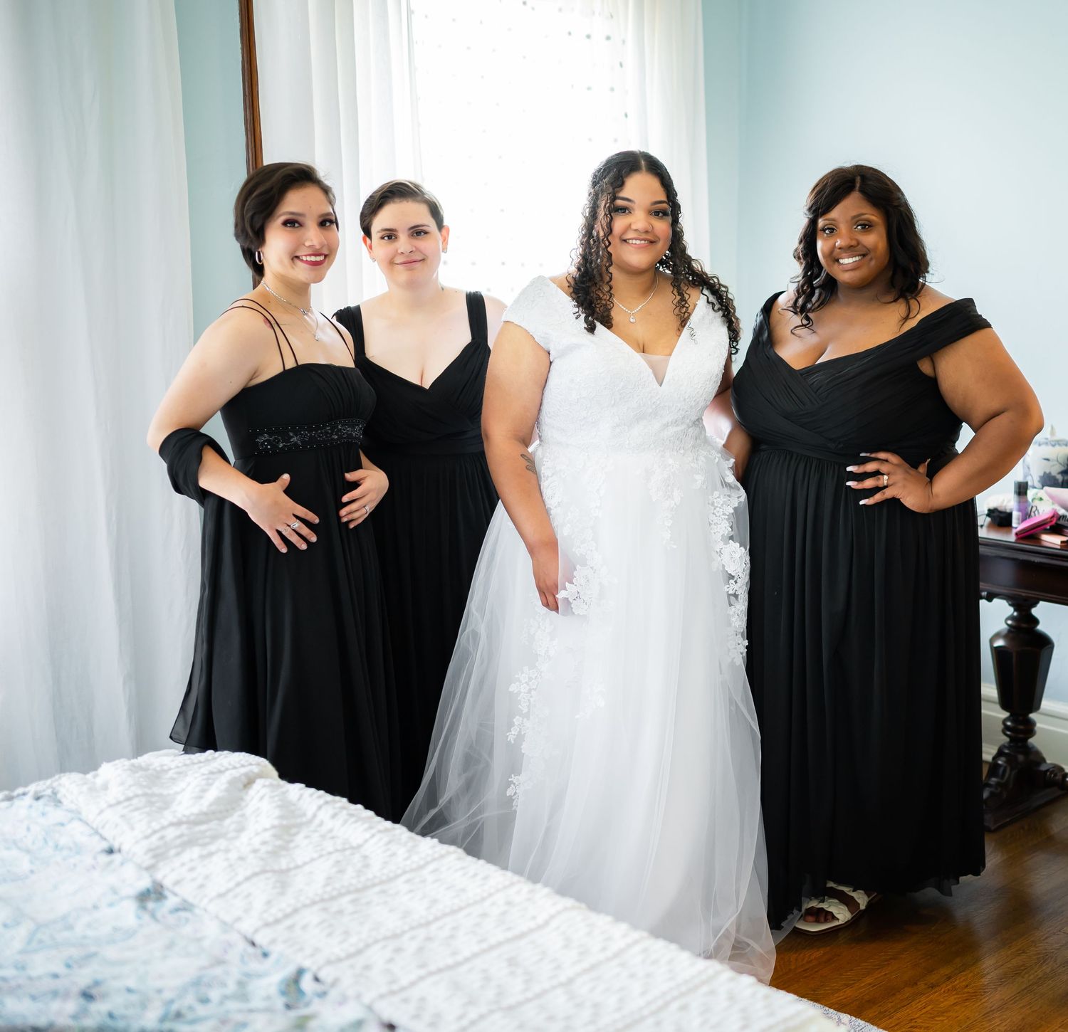 Wedding party wearing black dresses and white gown posing together in a bright room.
