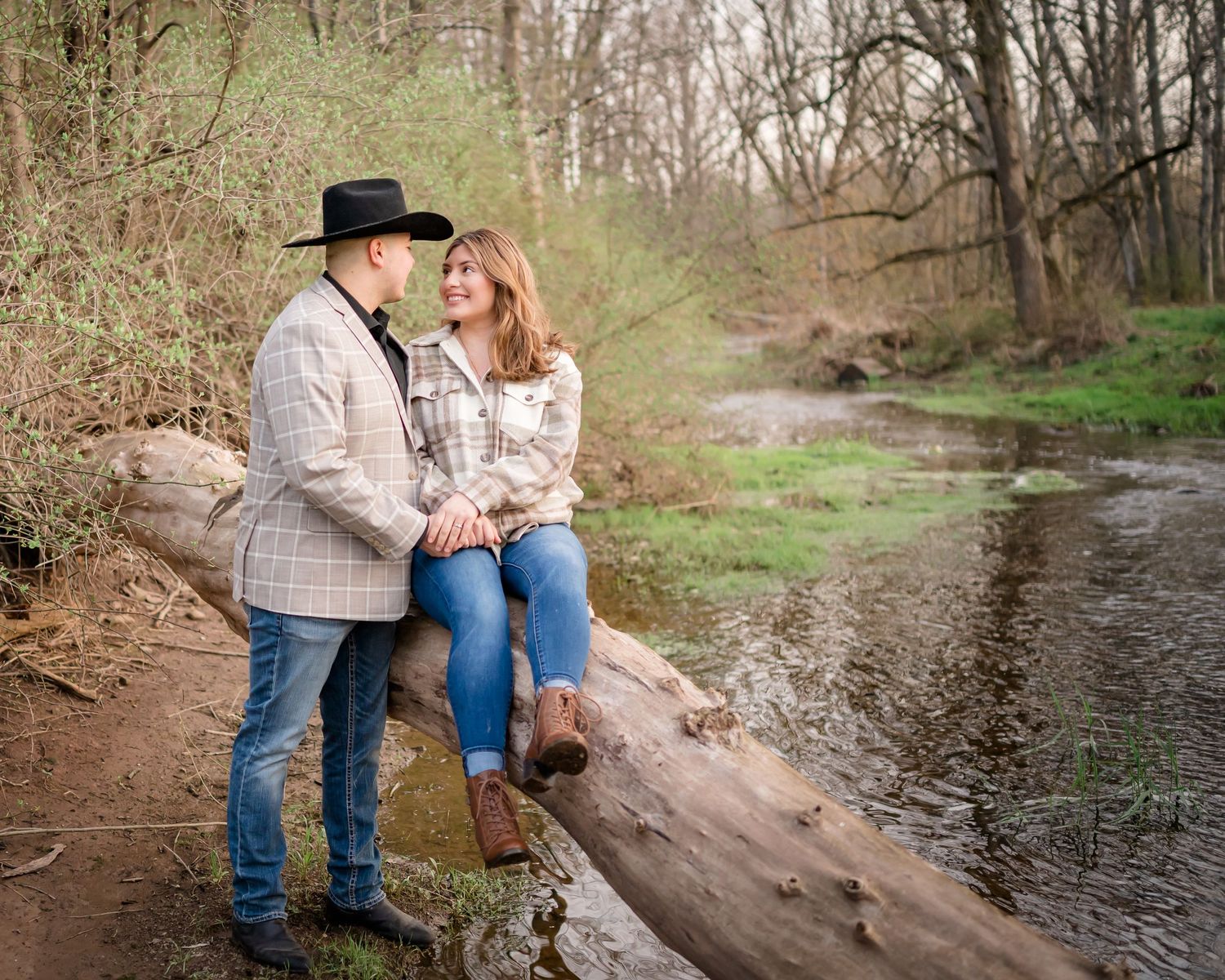 A couple sits romantically on a fallen tree trunk beside a flowing stream.