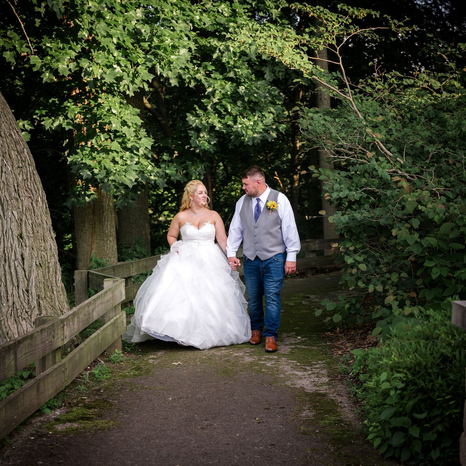 Wedding couple walking along a tree-lined path in a romantic woodland setting.