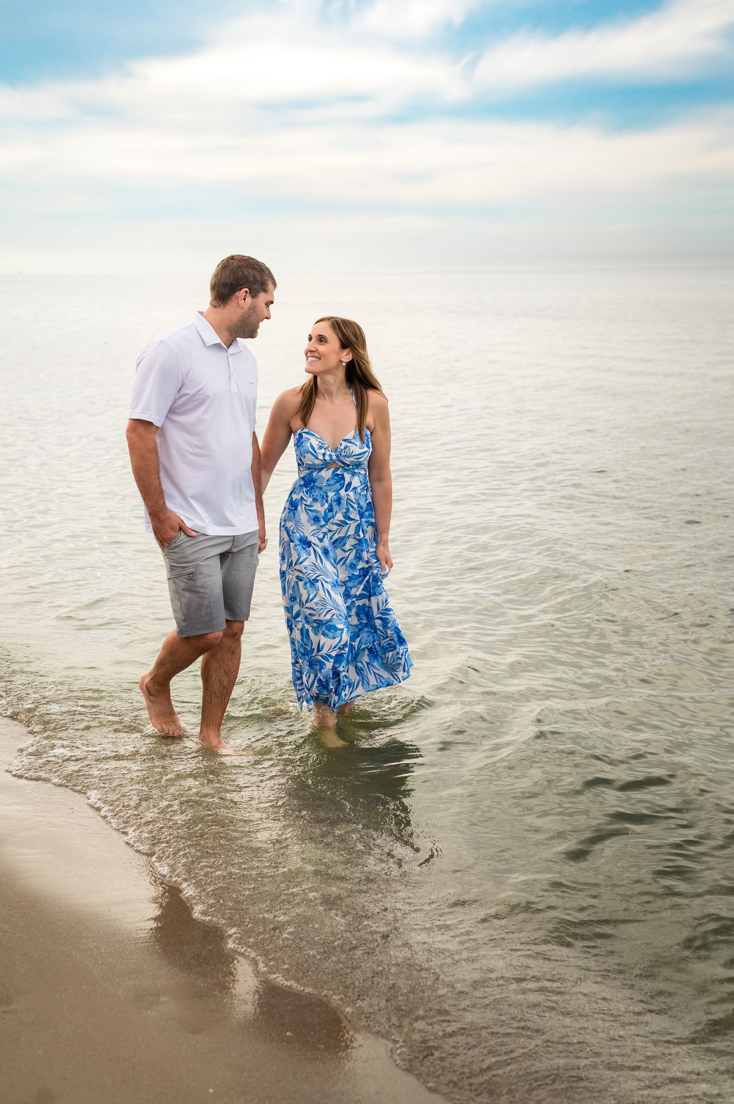 A couple wading in ocean waters wearing summer attire against a misty horizon.