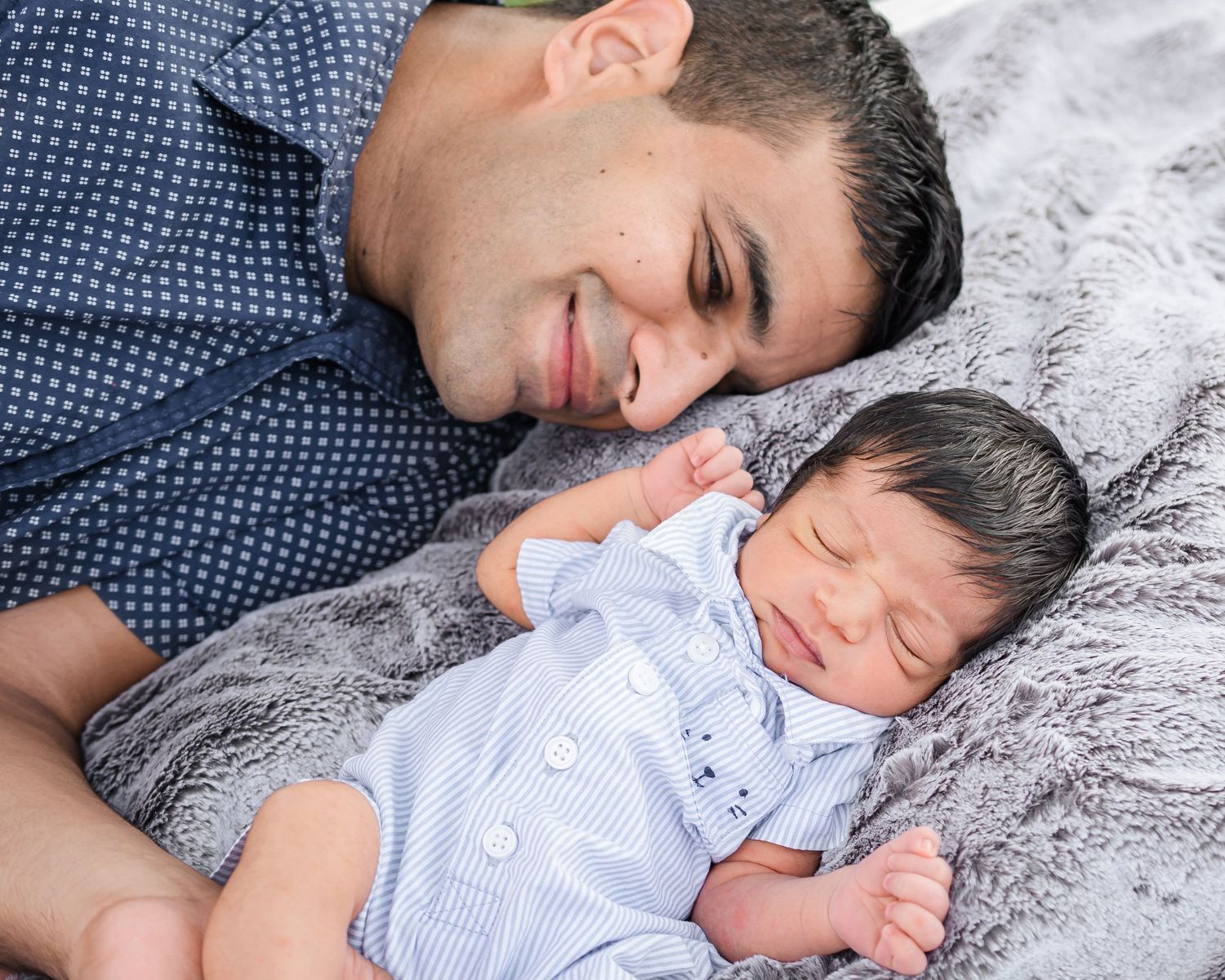 Parent and child sleeping peacefully together on soft gray bedding while wearing blue and white clothing.