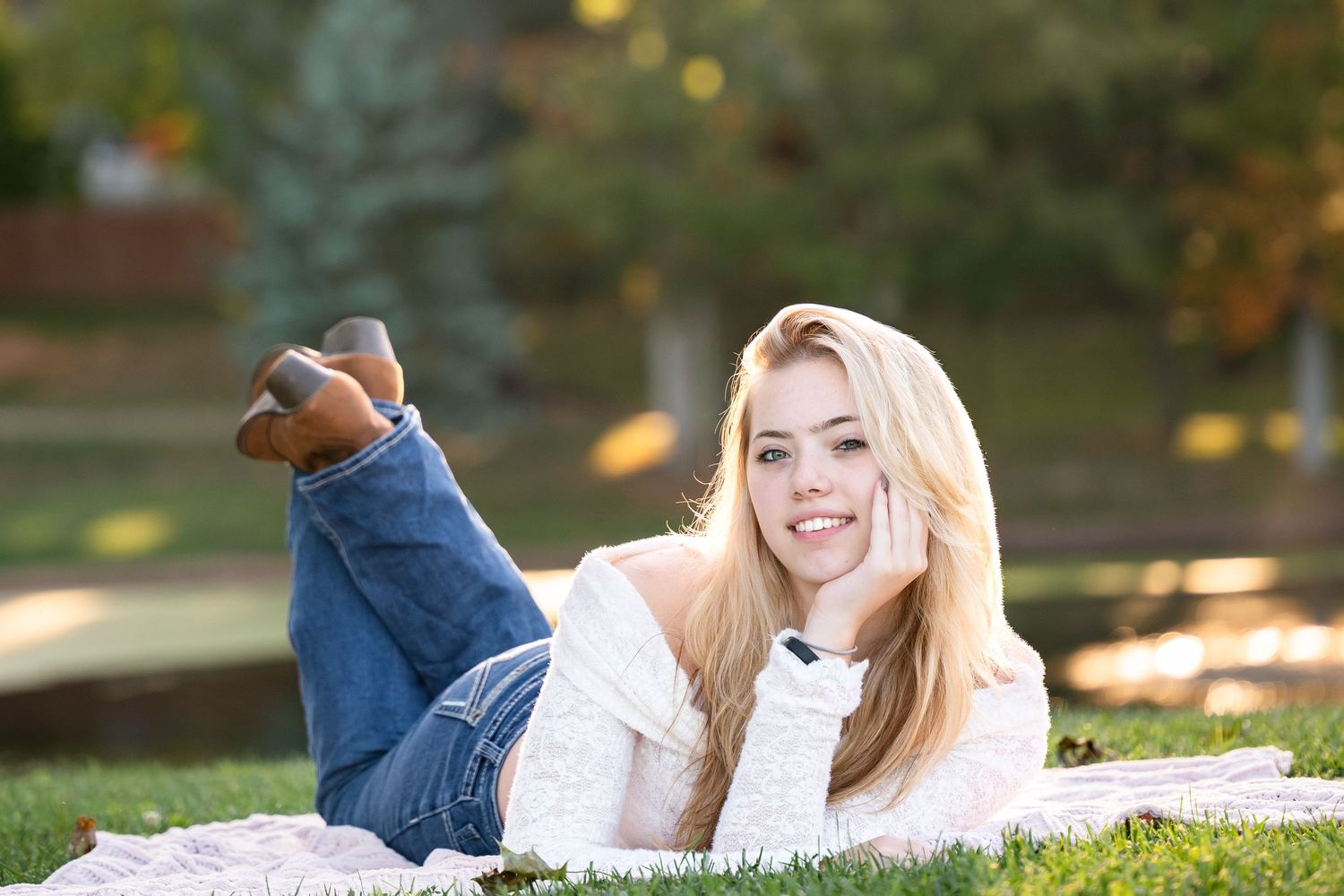 A person in casual attire lies on a blanket in the grass during autumn with golden light filtering through.