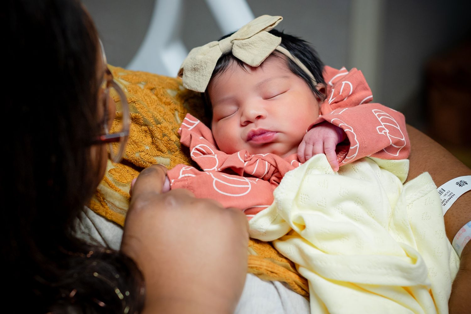 A sleeping newborn baby wrapped in yellow and pink blankets rests peacefully.