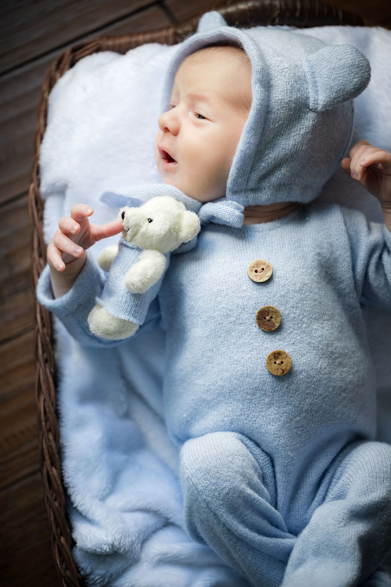 Sleeping baby wearing soft blue sweater with decorative buttons and small plush toy.