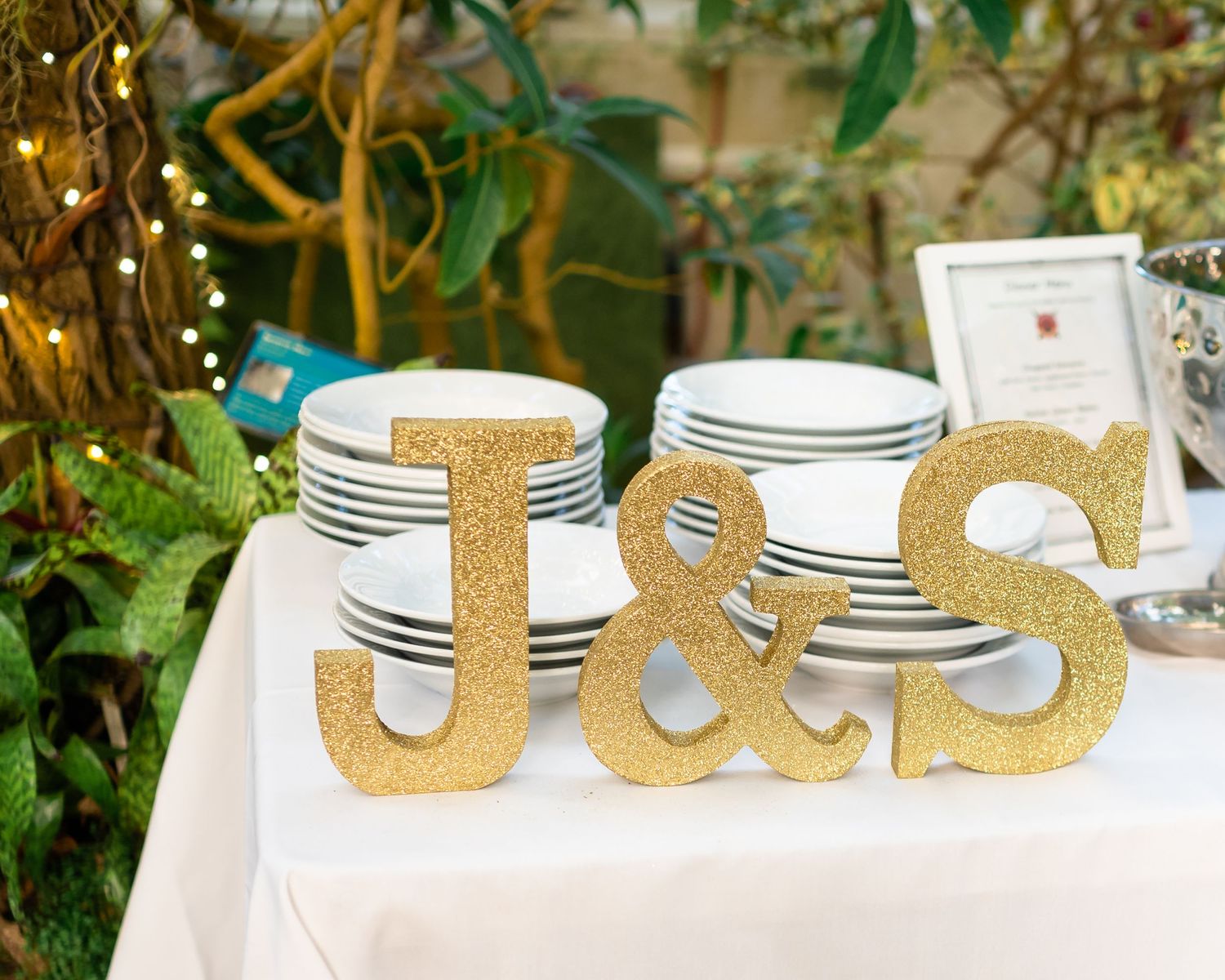 Gold glitter J&S letters displayed on white plates for wedding reception decor.