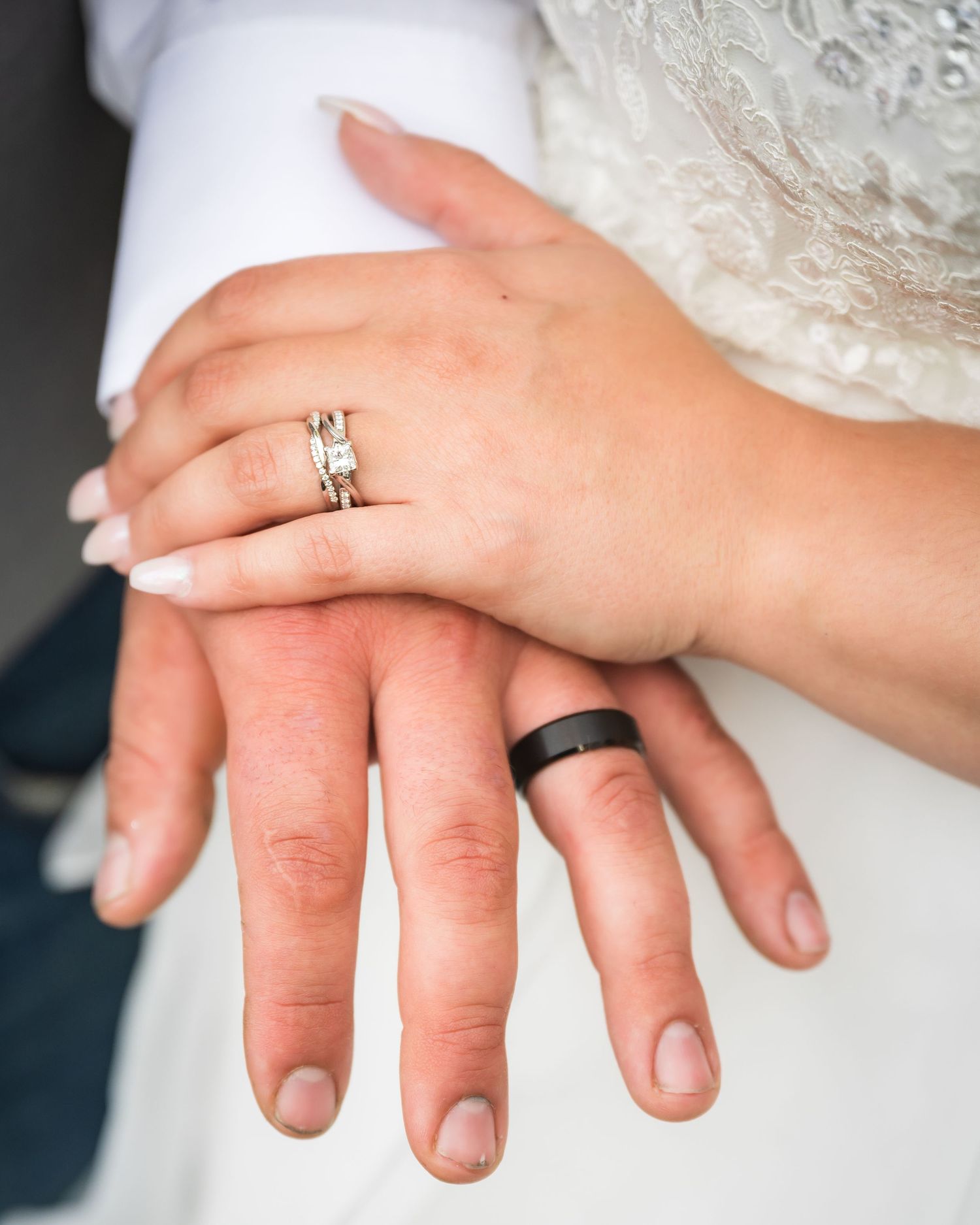 Close-up of newlywed hands displaying wedding rings against white fabric.
