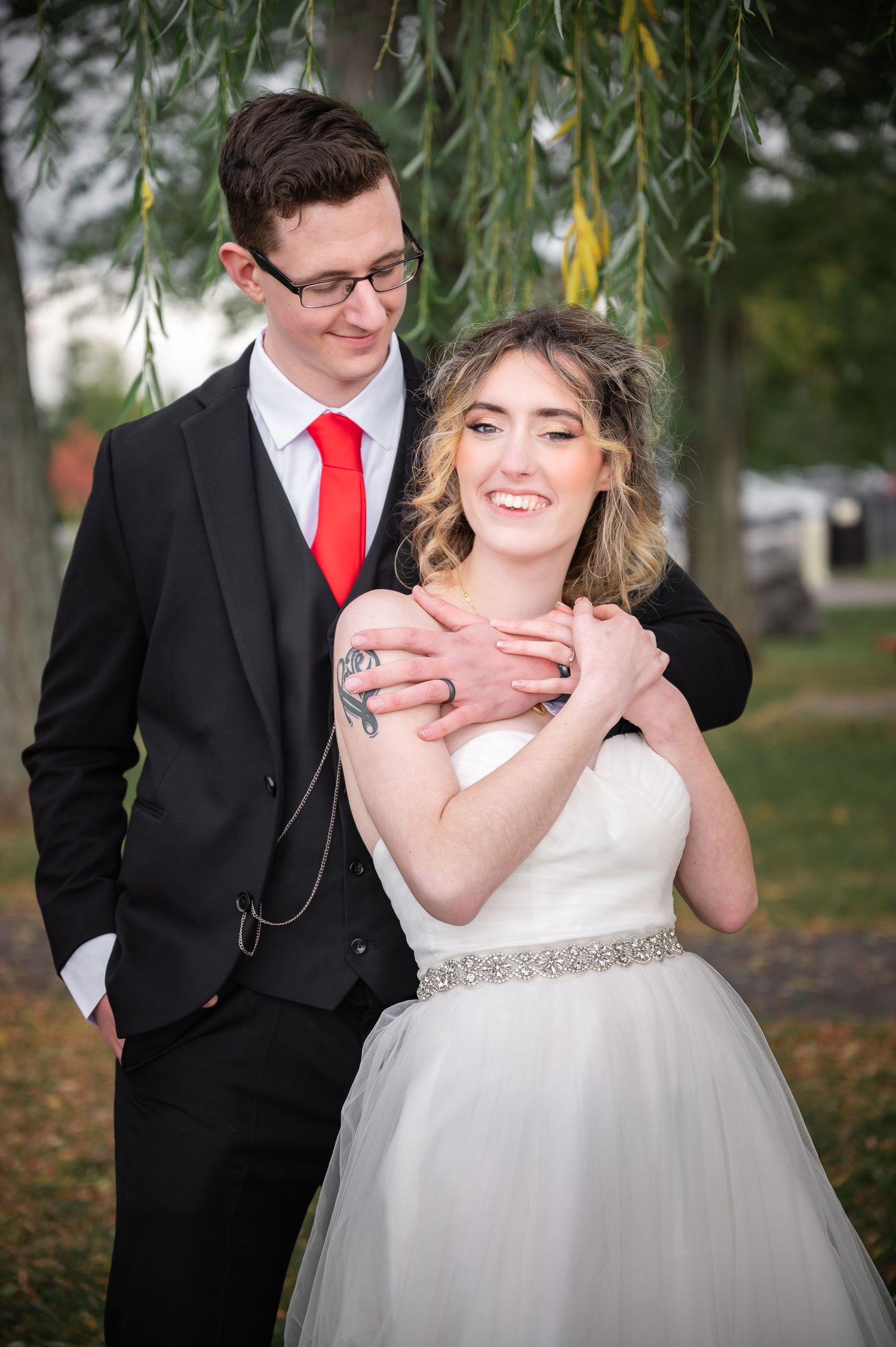 Romantic wedding photo of couple embracing under willow branches.