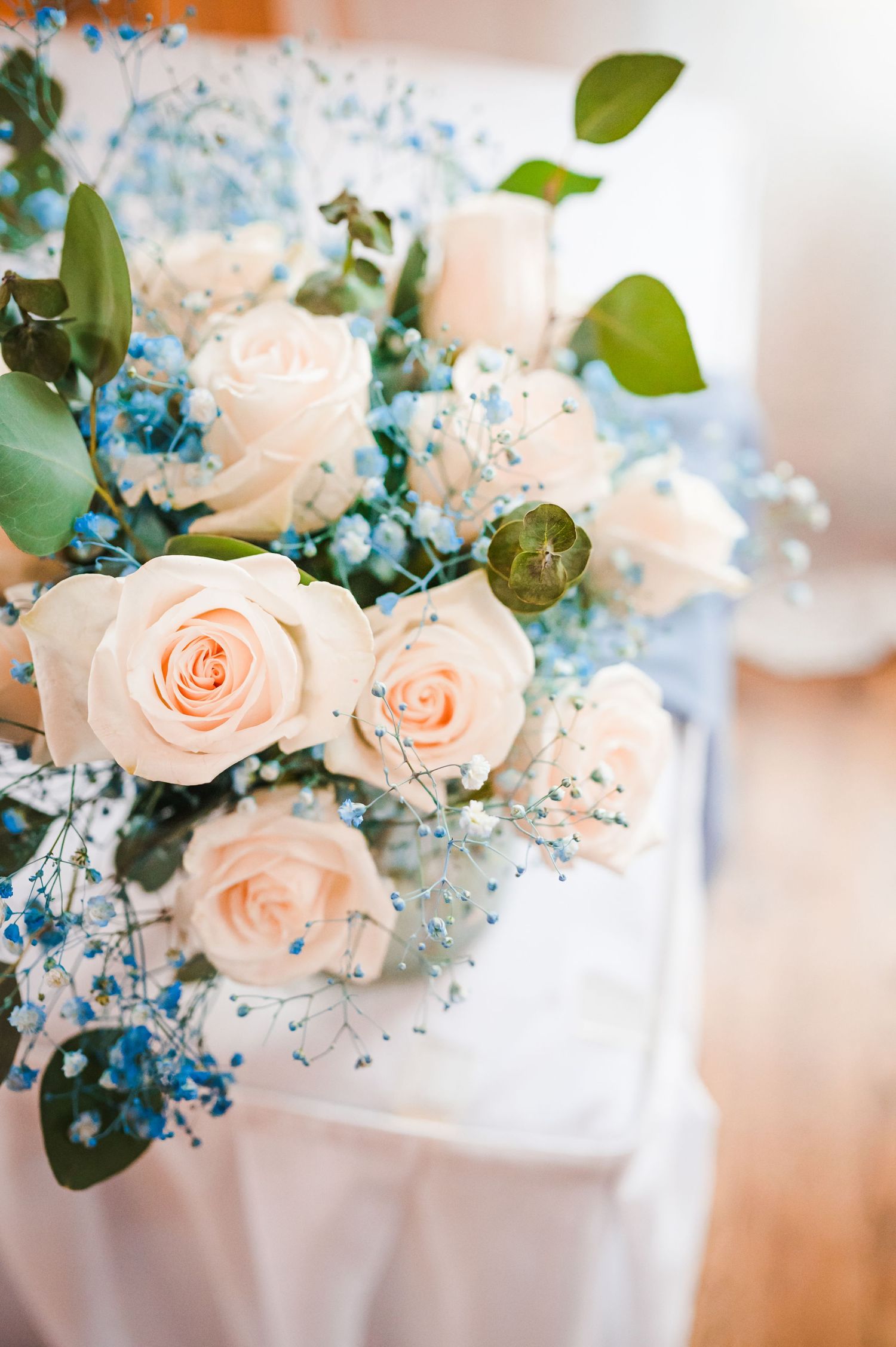 Elegant wedding bouquet featuring peach roses and blue baby's breath with green foliage.