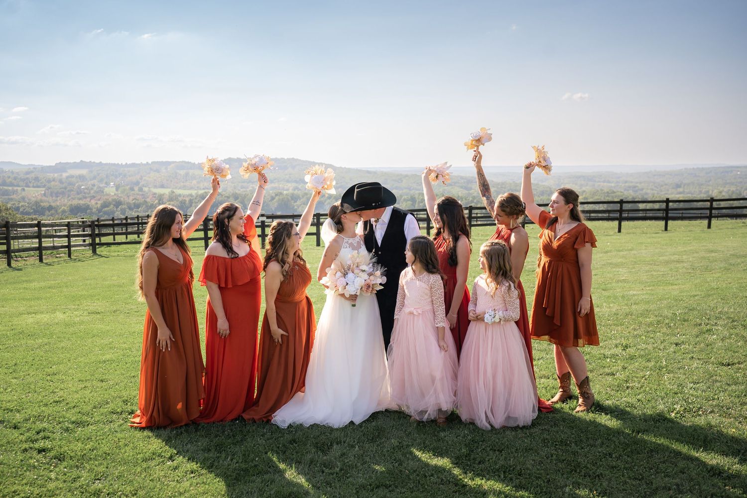 Wedding party in sunset landscape with bridesmaids in rust and pink dresses celebrating outdoors.