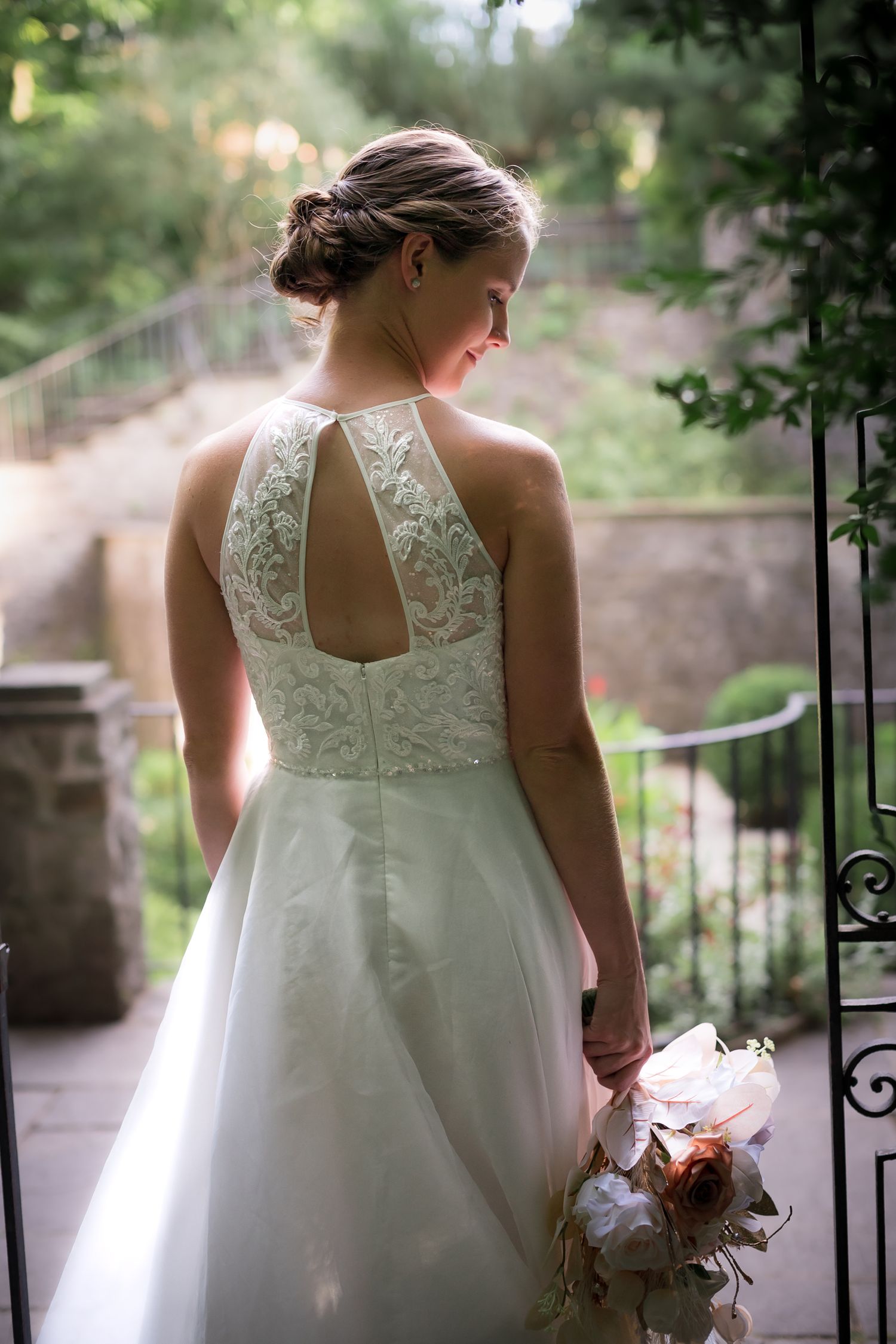Back view of a wedding dress with delicate lace details and keyhole back design in an outdoor garden setting.