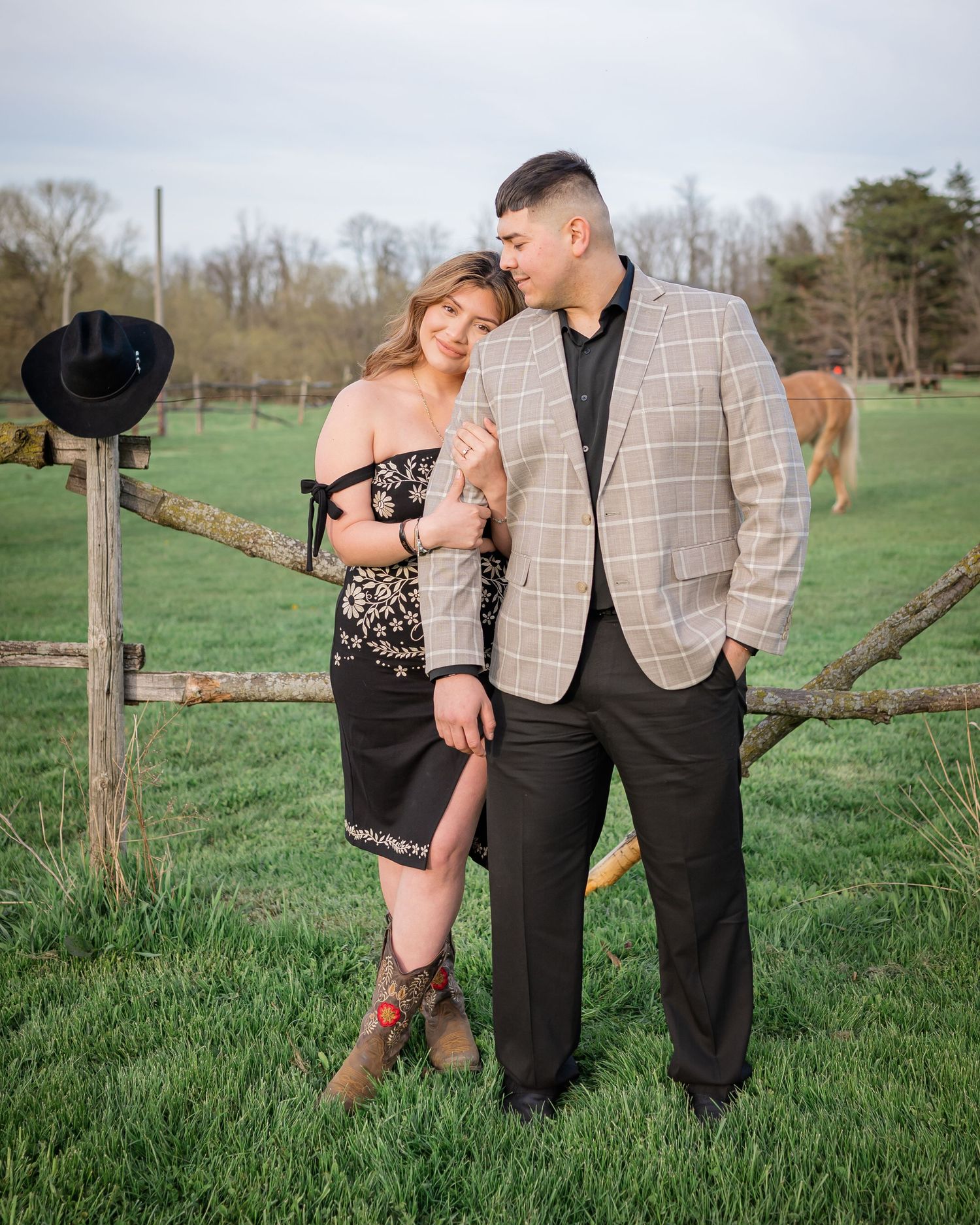 Couple in evening wear embracing in a scenic green field, creating a romantic outdoor photoshoot atmosphere.