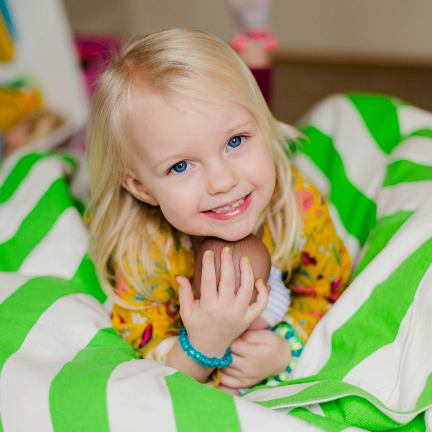Child resting on green and white chevron patterned cushions with colorful floral print clothing.