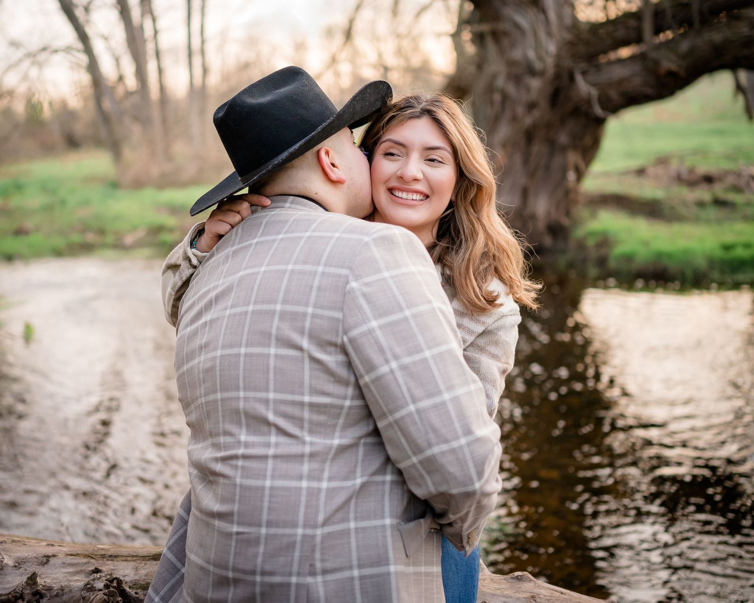 A tender moment shared between a couple by a stream with trees in the background.
