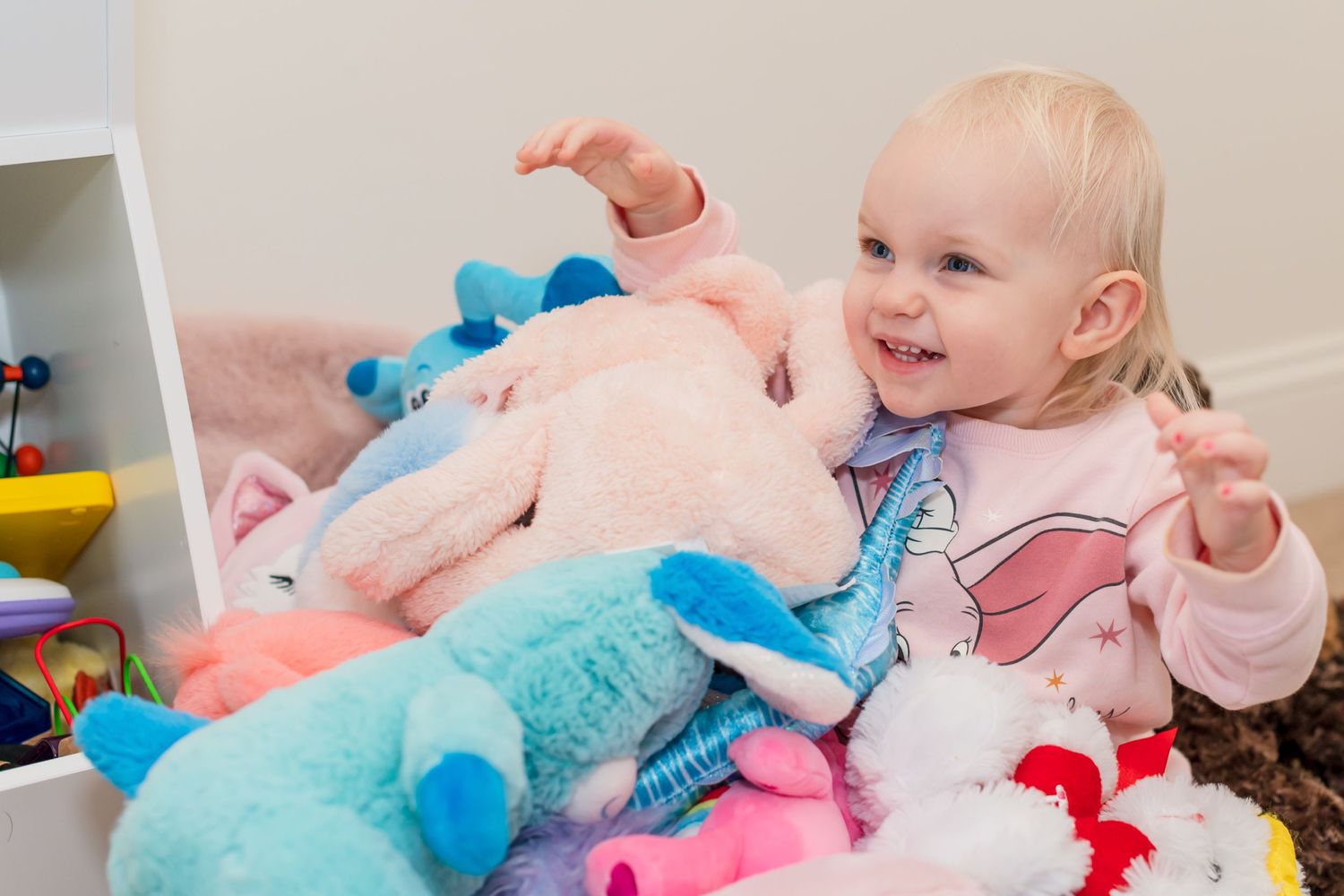 Child playing with colorful plush toys and stuffed animals in playroom.