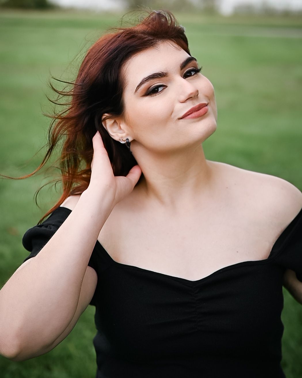 Portrait of a woman in black dress smiling outdoors with windswept hair and natural lighting.