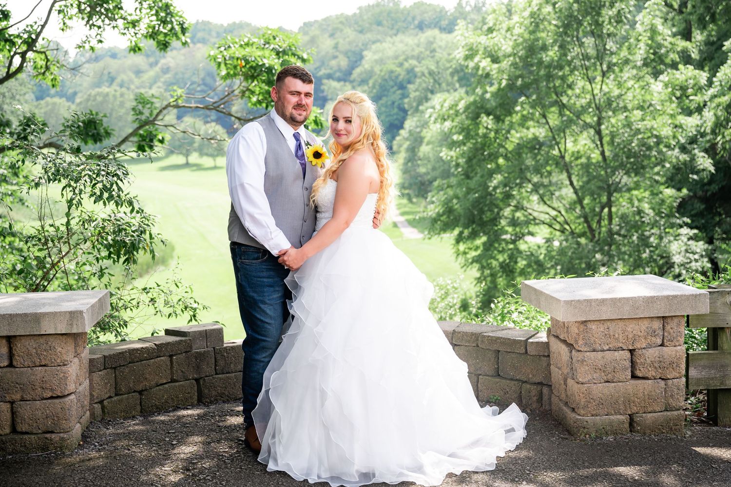 A romantic wedding portrait on stone steps overlooking a lush green valley background.
