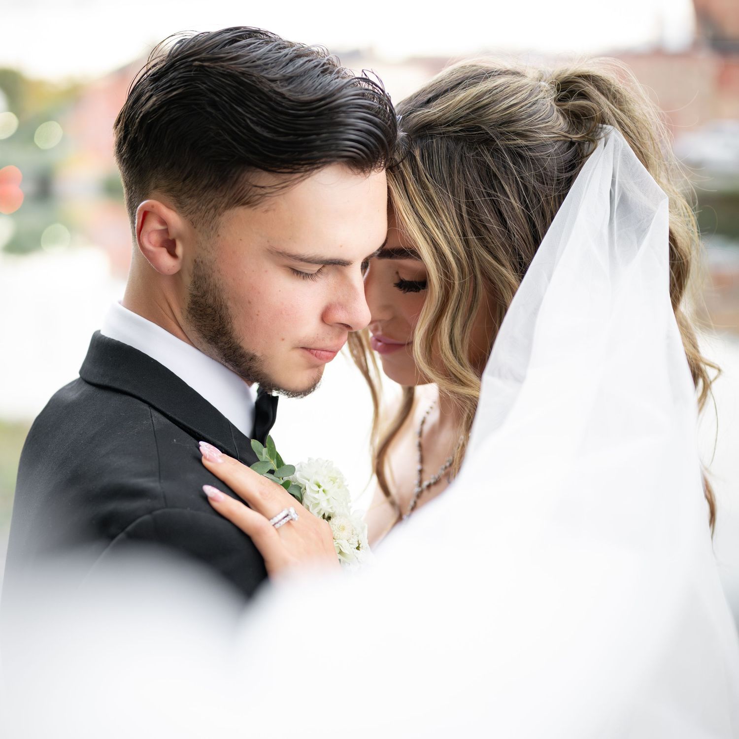 A romantic wedding couple embraces in soft natural light during their outdoor photoshoot.