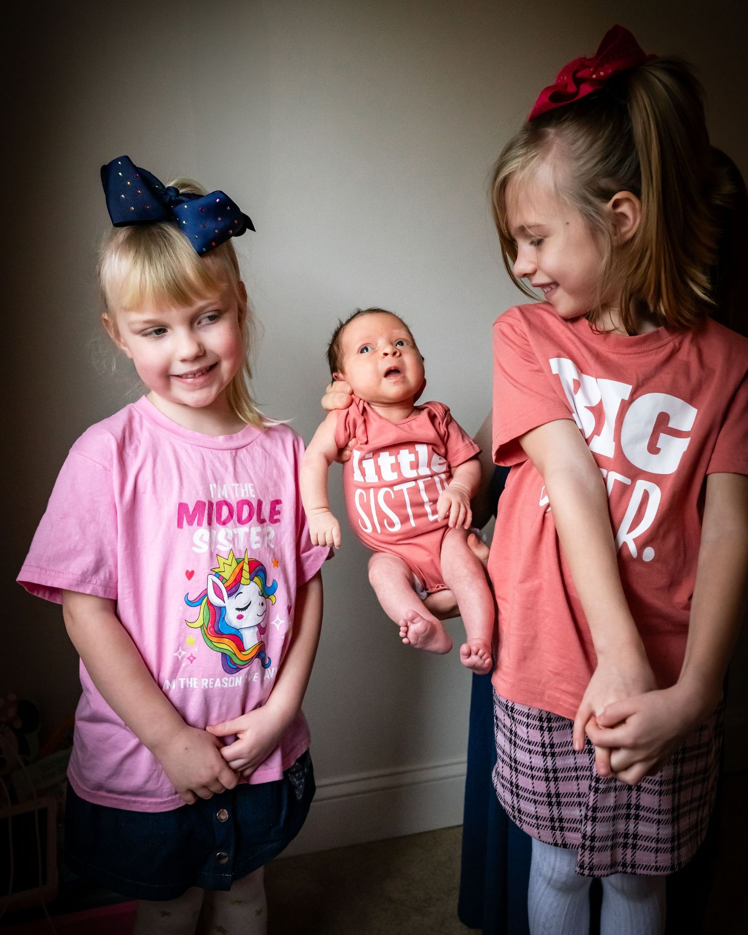 Three siblings wearing matching t-shirts with fun slogans pose together against a wall.