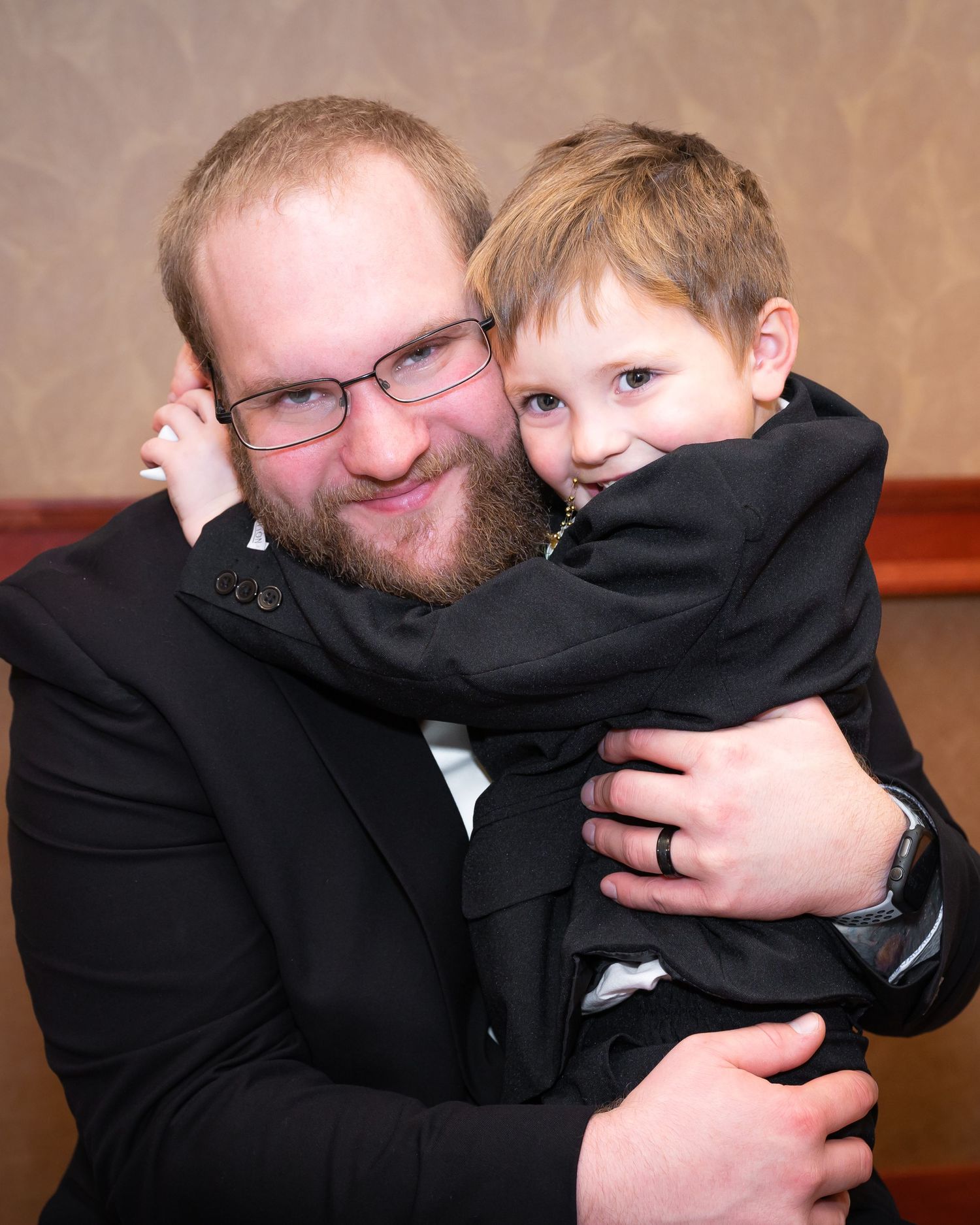 A heartwarming moment between a bearded man in glasses and a young boy in formal attire.