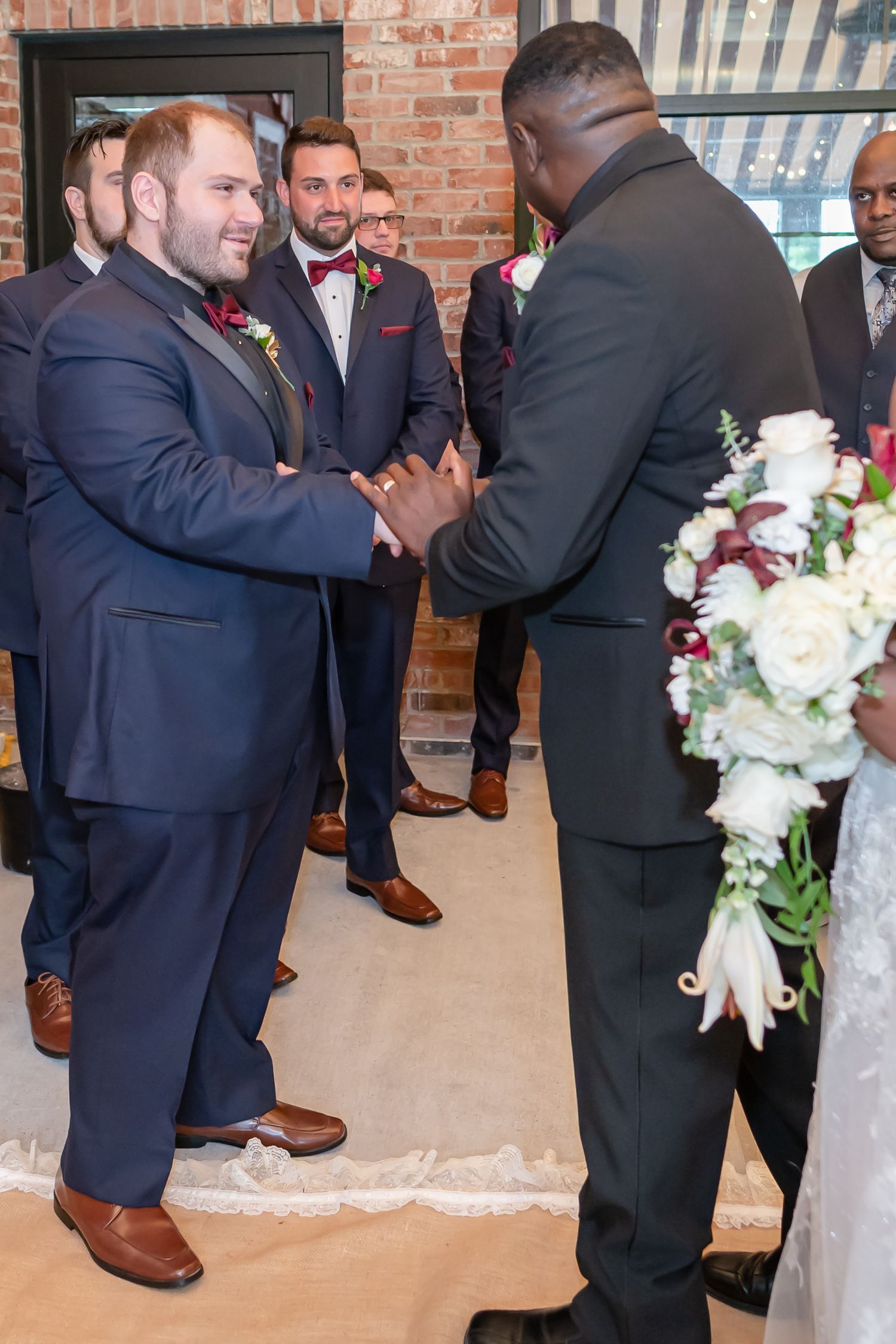 Wedding party members in navy suits exchanging greetings in front of a brick wall.