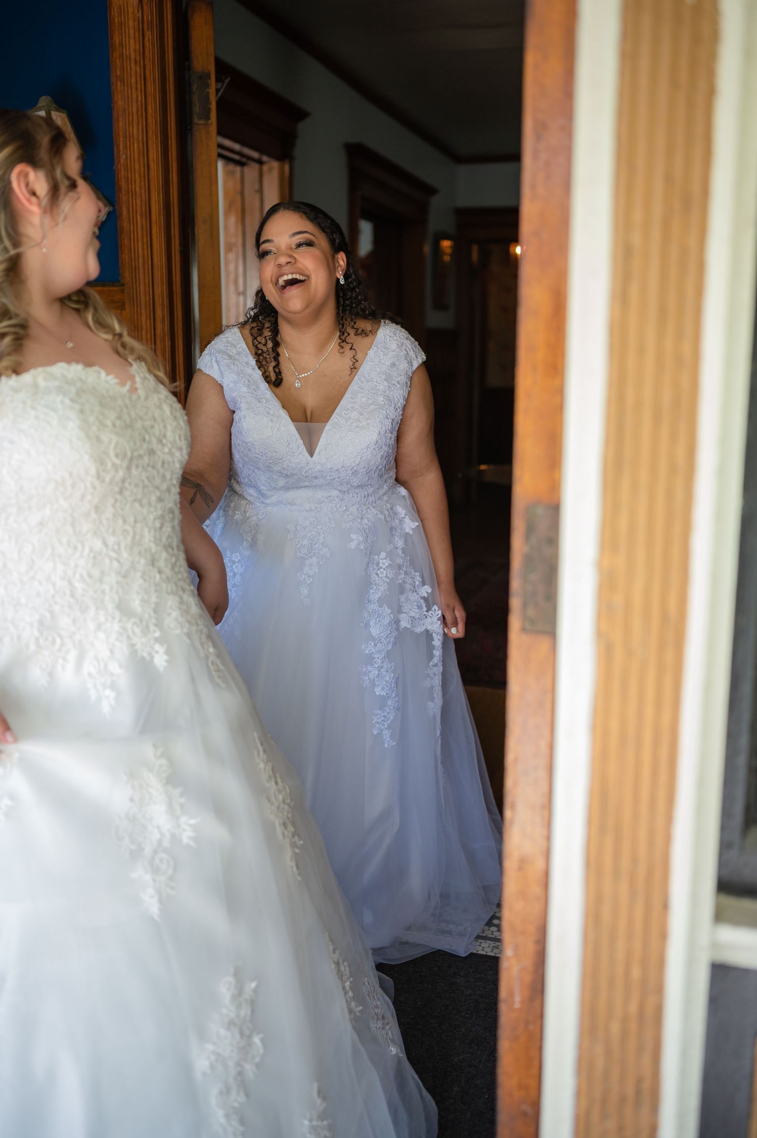 Two people in elegant white and lavender gowns sharing laughter in a doorway.