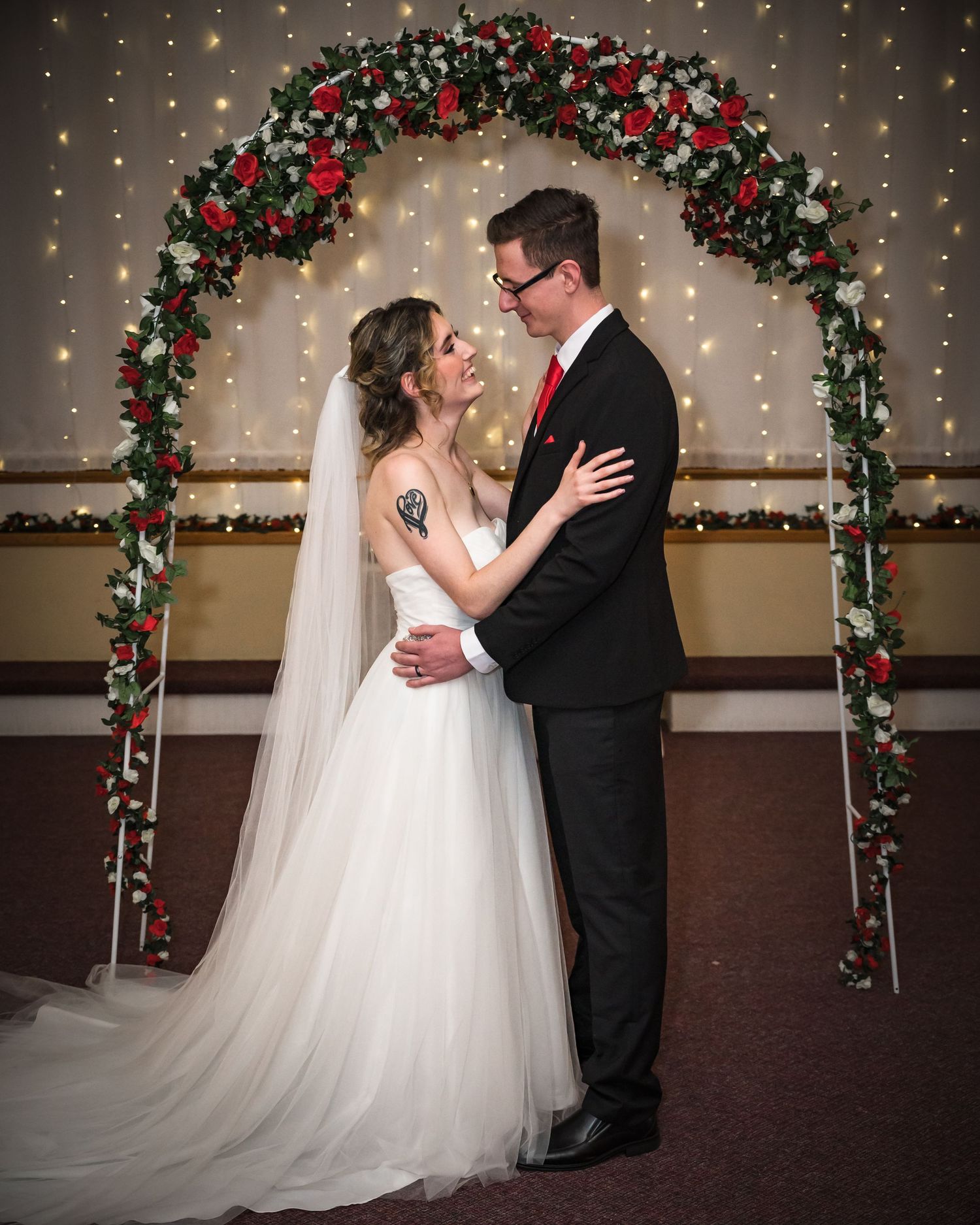 A wedding couple poses under a festive Christmas arch decorated with lights and greenery.