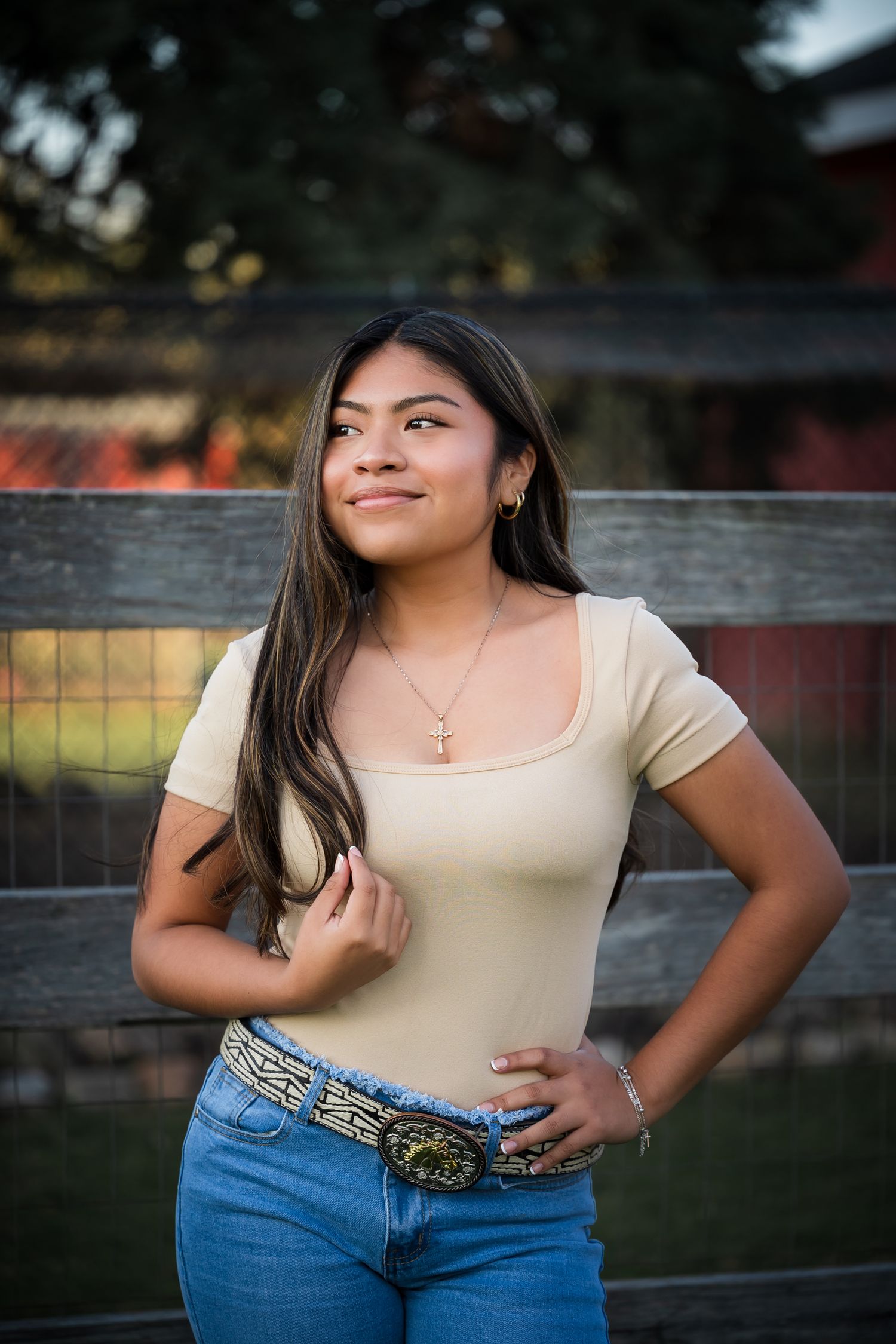 Outdoor portrait near a wooden fence showing a casual outfit with blue jeans and beige top at golden hour.
