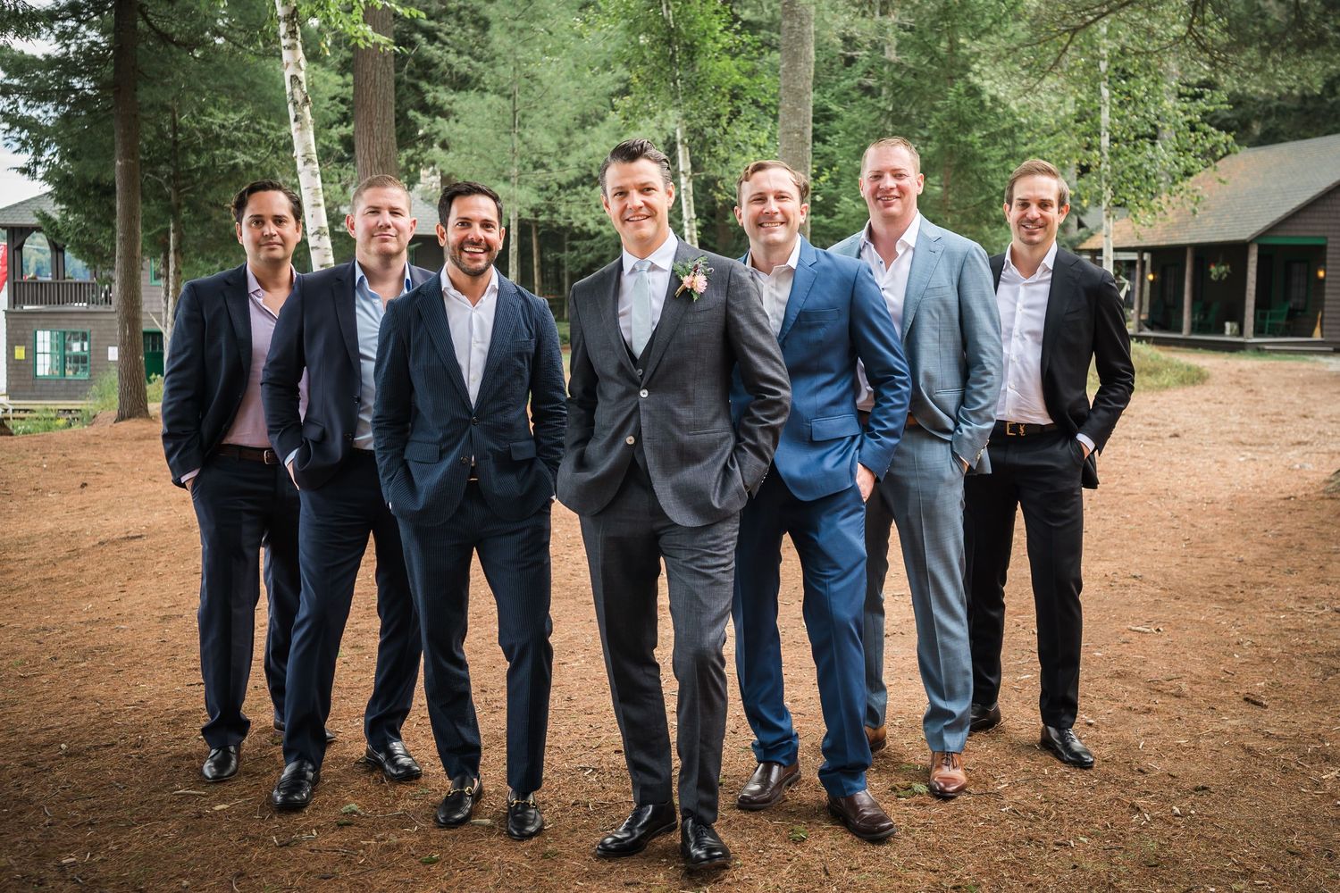 A series of five candid photos showing groomsmen in navy blue suits walking together outdoors in a rustic setting.