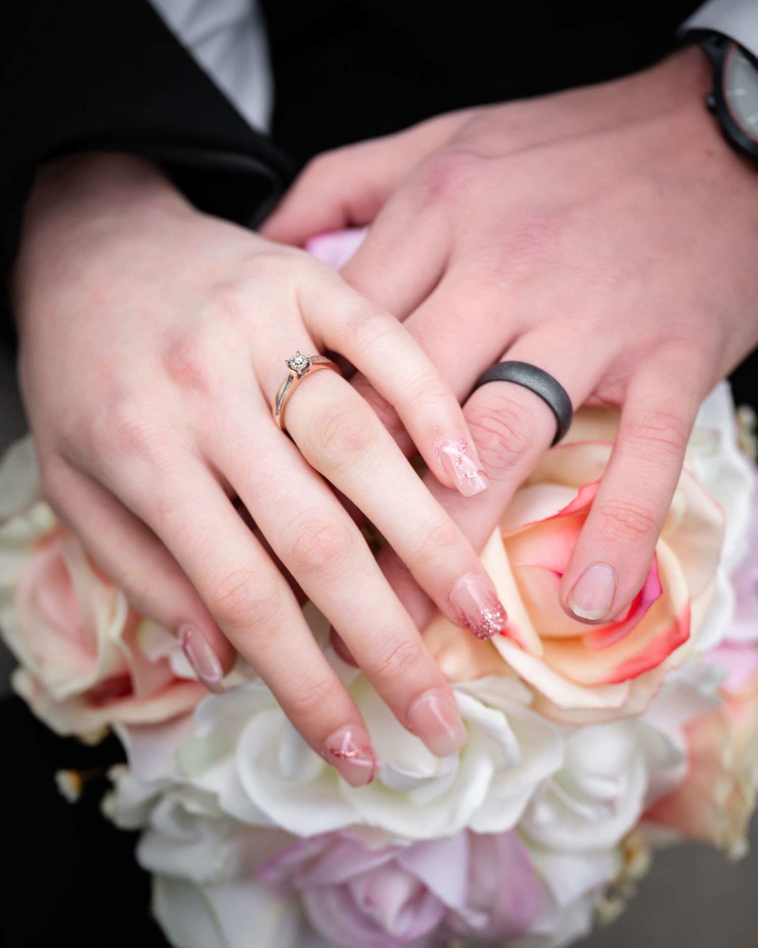 Close-up of hands showing wedding rings against pink and white roses.