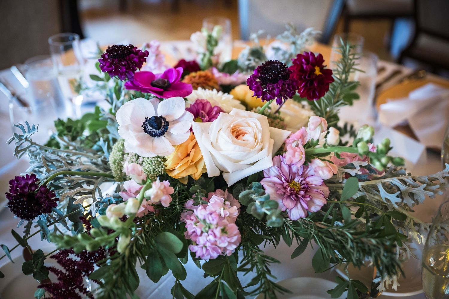 Vibrant wedding centerpiece with purple, pink and white flowers arranged with greenery.