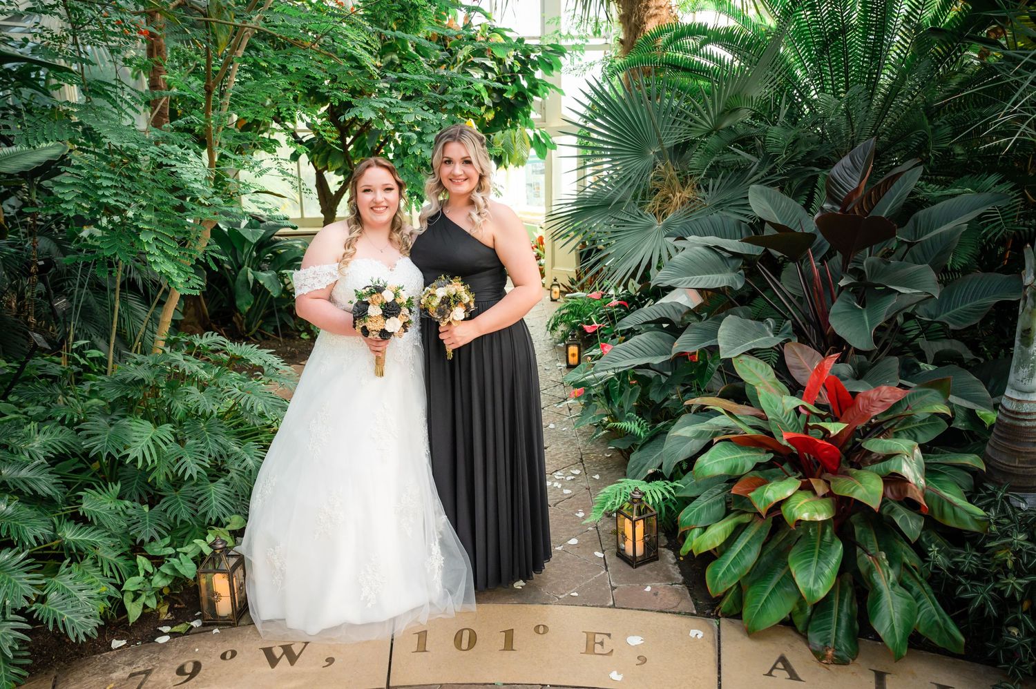 Garden wedding photo with tropical plants and lantern decorations on stone pathway.