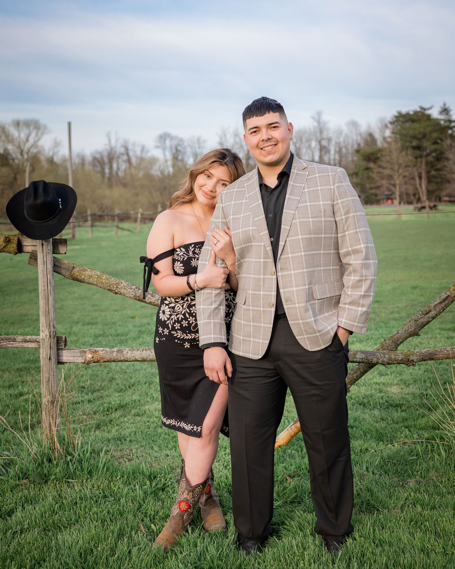 A couple poses together in a rustic farm setting with wooden fencing.
