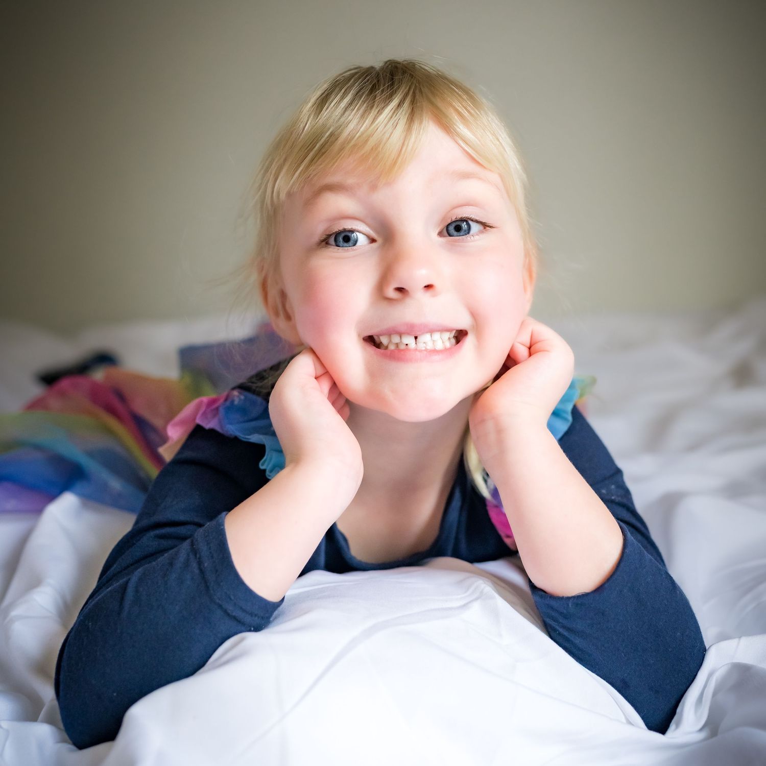 A sequence of five photos showing a child lying on white bedding in a navy blue shirt making playful expressions.