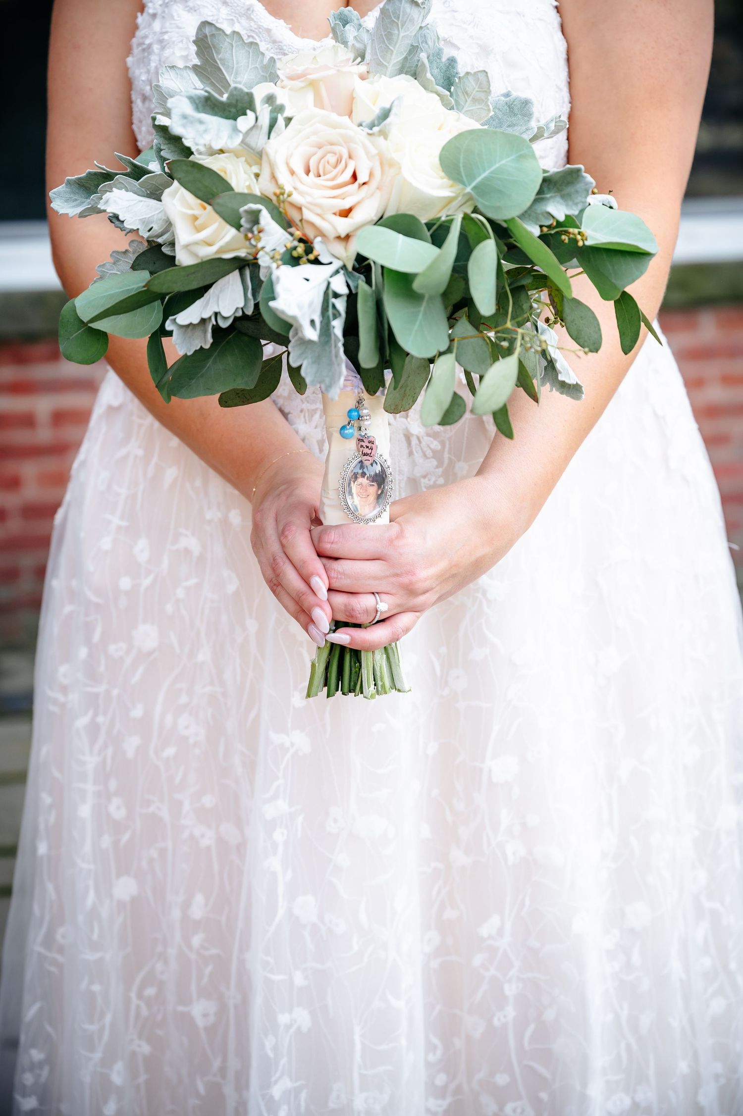 A bridal bouquet of blush roses and eucalyptus leaves held against a white lace wedding dress.
