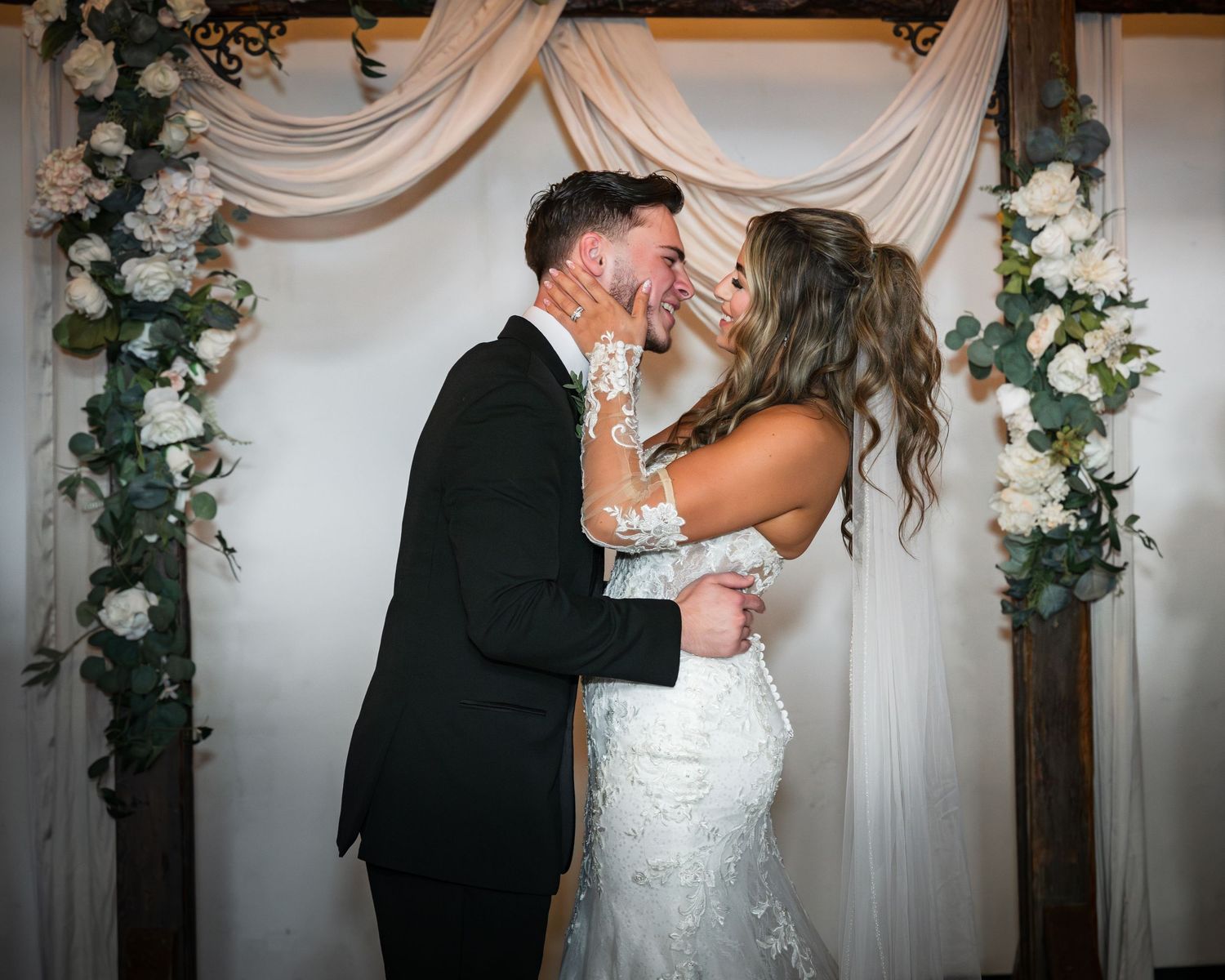 A romantic first dance moment between newlyweds at their wedding reception with white floral decor and drapery.