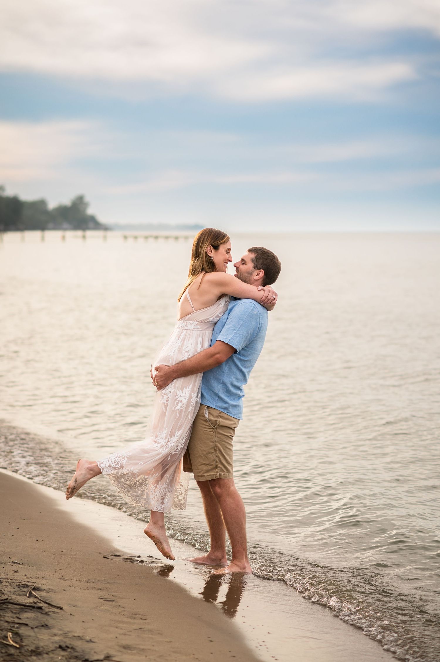 A romantic beach embrace at sunset with waves lapping at their feet.