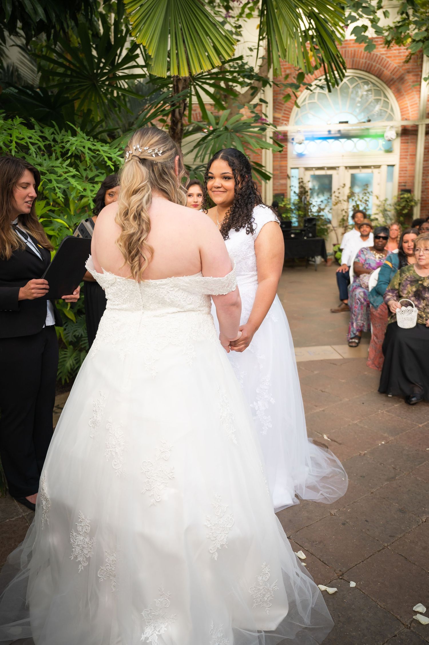 Wedding ceremony in a lush greenhouse with palm fronds and tropical plants.
